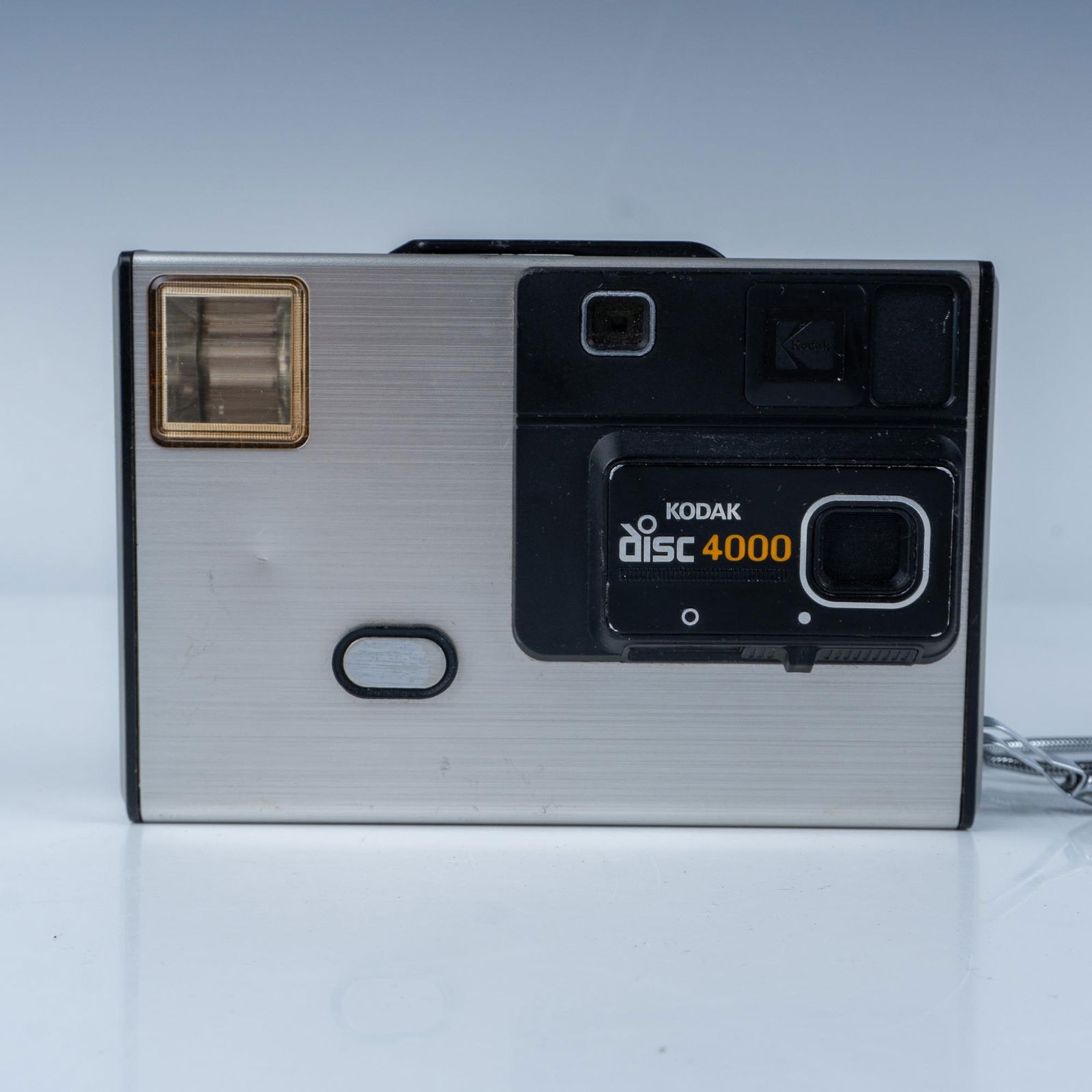 Kodak Disc 4000 Camera: Vintage Kodak Disc 4000 camera, manufactured by Eastman Kodak Company, featuring a sleek silver and black design with built-in flash and wrist strap for portability. This retro camera is an excellent