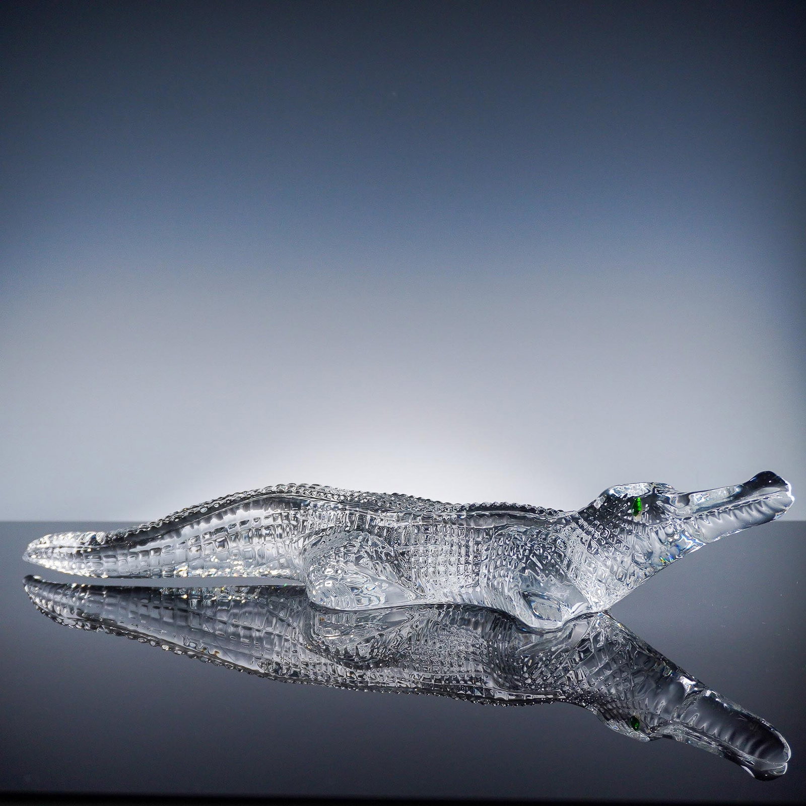 Baccarat Crystal Alligator Sculpture: Baccarat crystal alligator sculpture featuring a highly detailed body with textured scales and a single striking green eye. Crafted in clear French crystal, this elegant figure captures the distinctiv