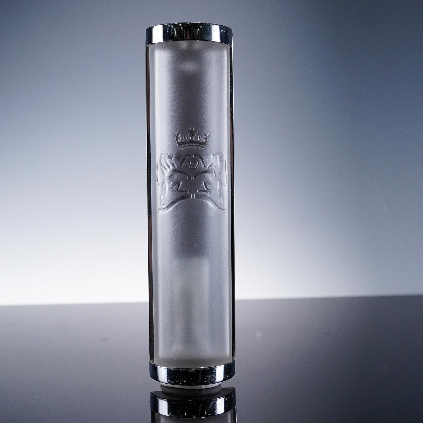 Lalique Crystal Mezuzah with Original Box: This elegant Lalique crystal Mezuzah features a frosted cylindrical body framed by polished chrome end caps. The front is beautifully etched with a crowned lion motif, symbolizing strength and divine 