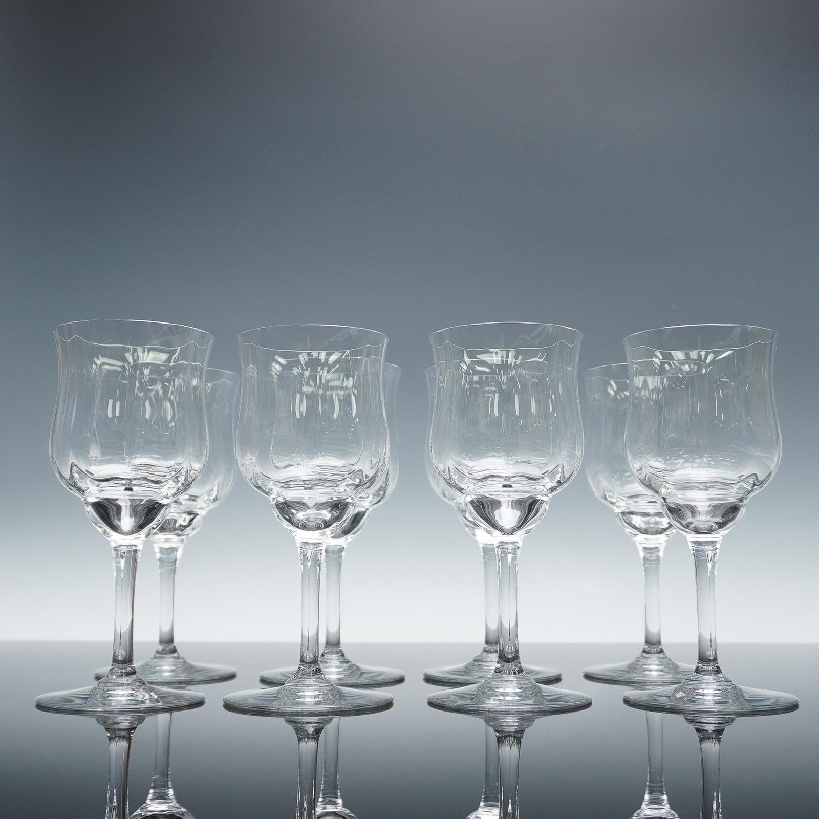 8pc Baccarat Crystal Wine Glasses, Capri: Set of 8 stylish clear crystal wine glasses in the Capri pattern. Each glass features a flared, tulip shaped bowl with a thick rounded base leading to a slender stem and circular foot. The elegant, su