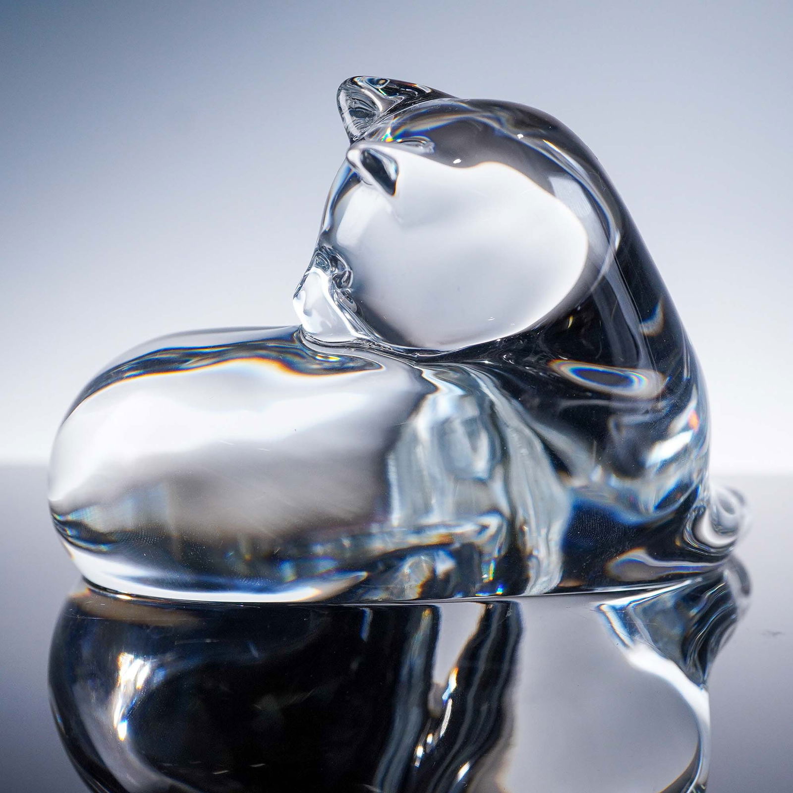 Baccarat Crystal Figurine, Reclining Cat: This elegant Baccarat crystal figurine portrays a reclining cat in a tranquil pose, rendered with smooth curves and a fluid silhouette that reflects the feline's calm grace. Crafted in clear French cr