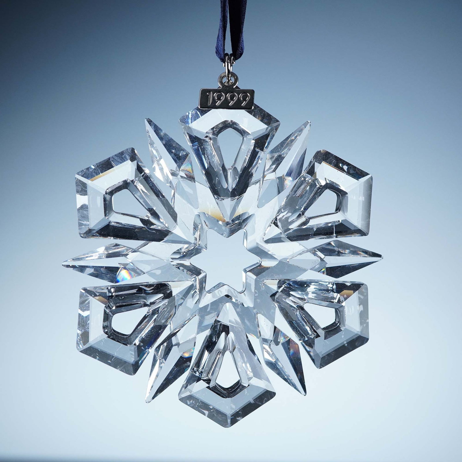 Swarovski Crystal Ornament, 1999 Christmas: This retired Swarovski 1999 Annual Edition Christmas Ornament features a radiant 12-point faceted clear crystal snowflake with bold, angular facets and a 1999-etched metal tag. The ornament is suspend
