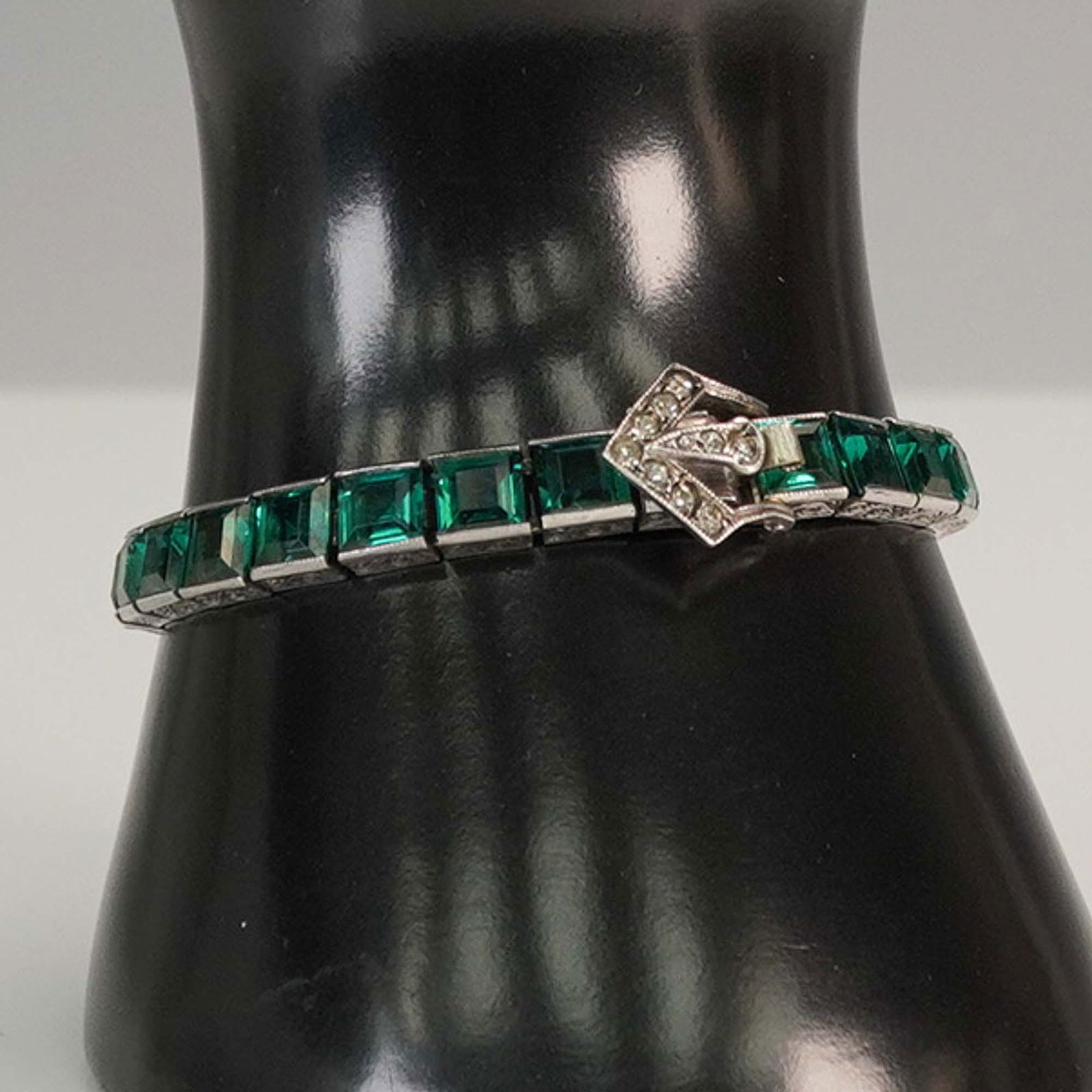 DiamonBar Sterling Silver Green Stone Line Bracelet: Art Deco style line bracelet by DiamonBar featuring a row of deep green emerald-cut stones set in sterling silver, finished with a stylized buckle clasp accented with clear stones. The clasp is marked