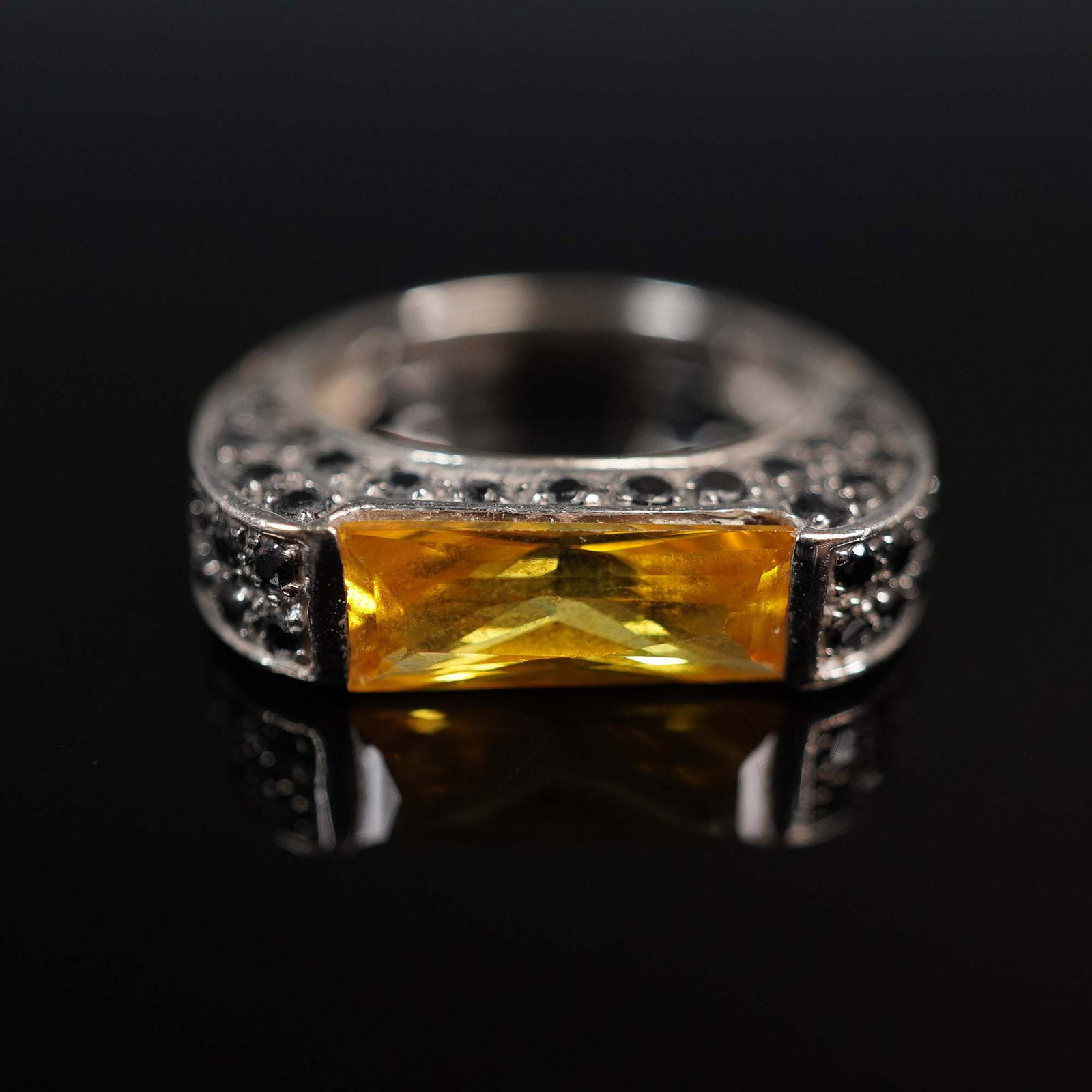 14K White Gold and Stone Modernist Ring: Elegant 14K white gold ring featuring a rectangular faceted golden-yellow stone, bezel set horizontally across the front. The setting is accented with pave-style black stones along the broad, modern b