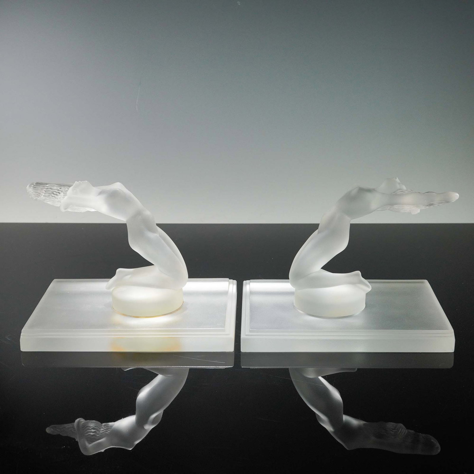 3pc Lalique Crystal Bookends, Chrysis: The piece portrays a stylized nude female figure kneeling with arms extended behind and head arched upward, sculpted with aerodynamic curves and simplified features in the Art Deco style. Formed in sa