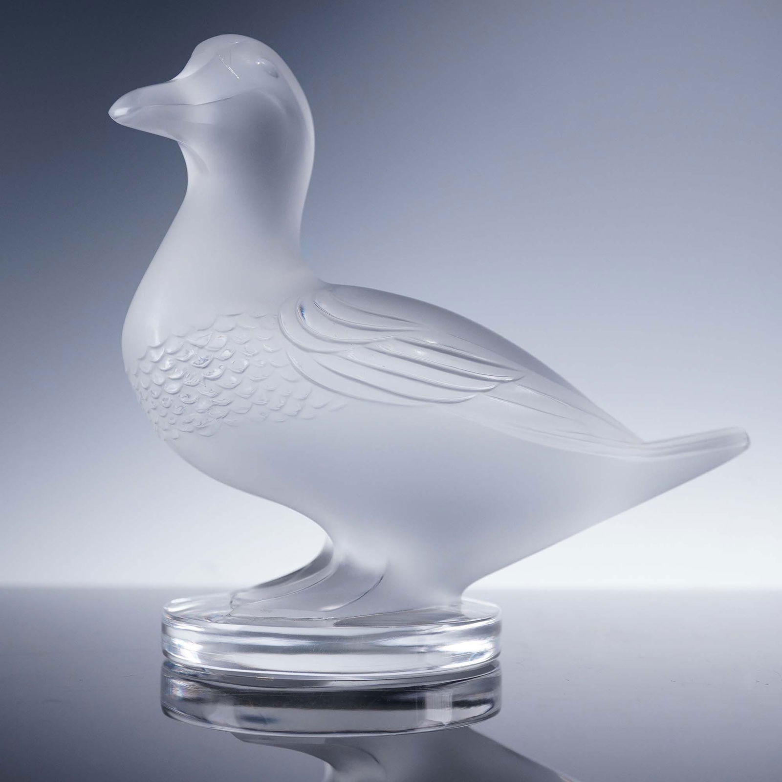 Lalique Crystal Figurine, Gedeon Duck: A crystal figure of a duck, executed in frosted and clear crystal with sculpted plumage and softly contoured form. The duck stands upright on a circular base, with textured feather detail across the b