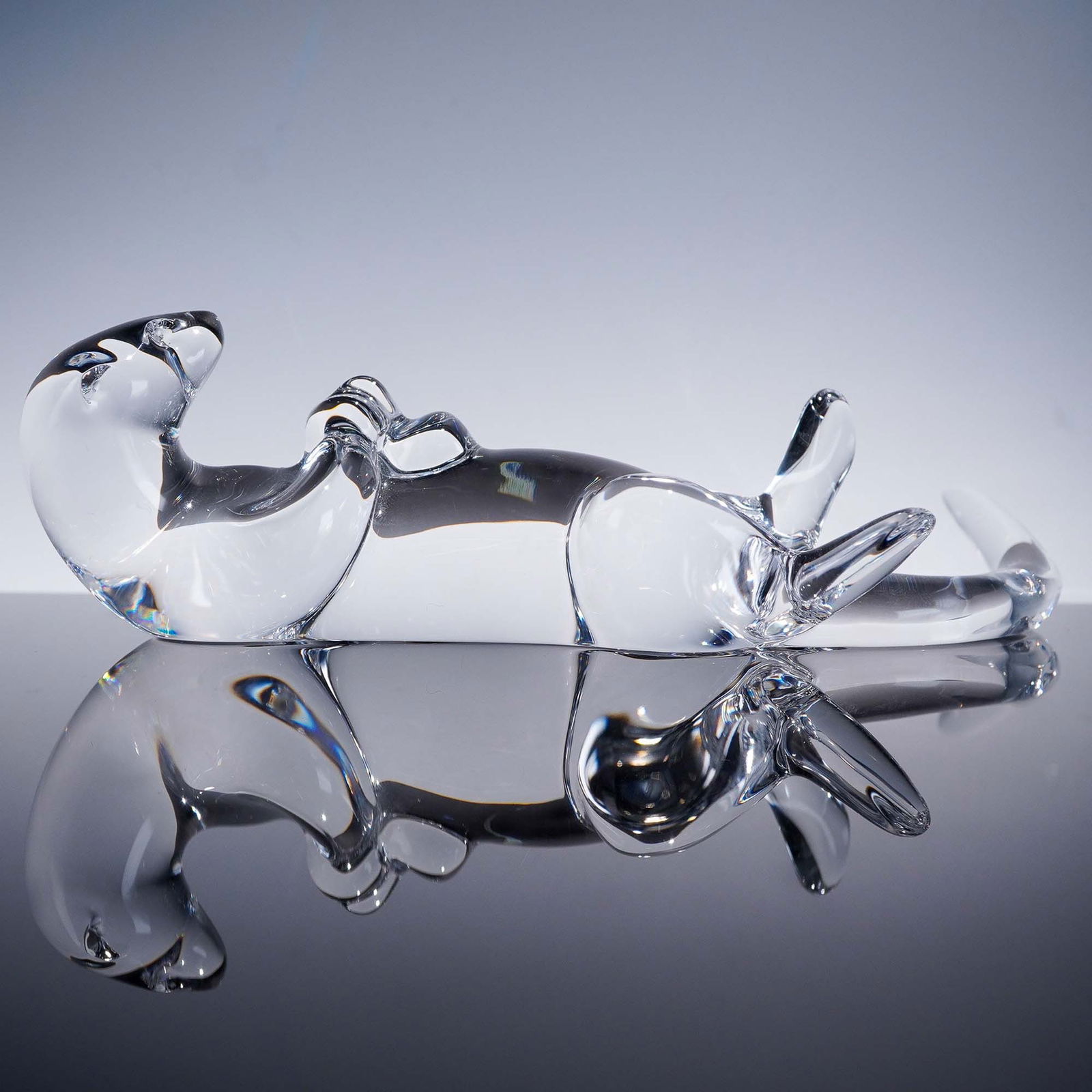 Baccarat Crystal Figurine, Reclining Otter: This striking Baccarat crystal figurine features a smooth, stylized depiction of a reclining otter, showcasing the brand's signature clarity and fluid artistry. The elegant lines and minimalist form c