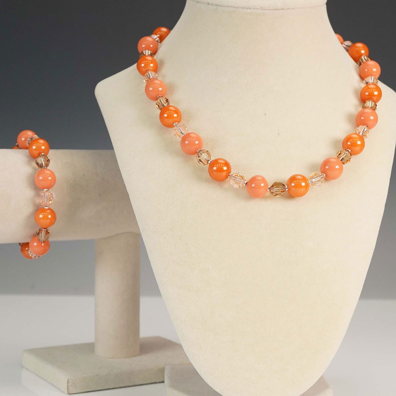 2pc Orange Bead and Crystal Necklace and Bracelet Set: Vibrant 2-piece jewelry set featuring a necklace and matching bracelet composed of glossy orange beads paired with faceted light peach crystals. Both pieces are completed with silver-tone toggle clasp