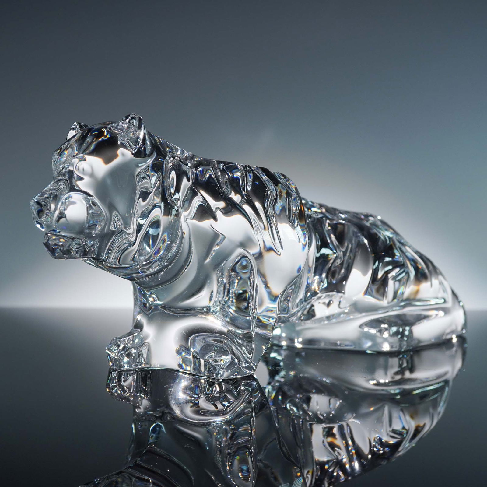 Baccarat Clear Crystal Figurine, Tiger: Striking clear crystal tiger figurine by Baccarat, meticulously crafted to capture the muscular power and fluid motion of a resting big cat. The detailed fur texture and expressive face highlight Bacc
