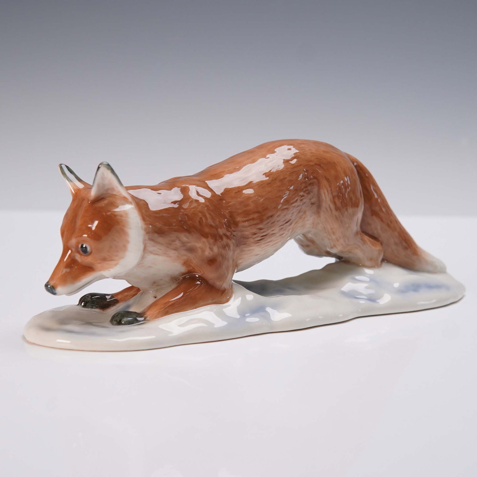 Royal Copenhagen Porcelain Figurine, Crawling Fox: Royal Copenhagen porcelain figurine depicting a red fox in a stalking, low-crawling pose. The figure is hand-painted in warm chestnut tones with subtle white and black accents, capturing the alert, fo
