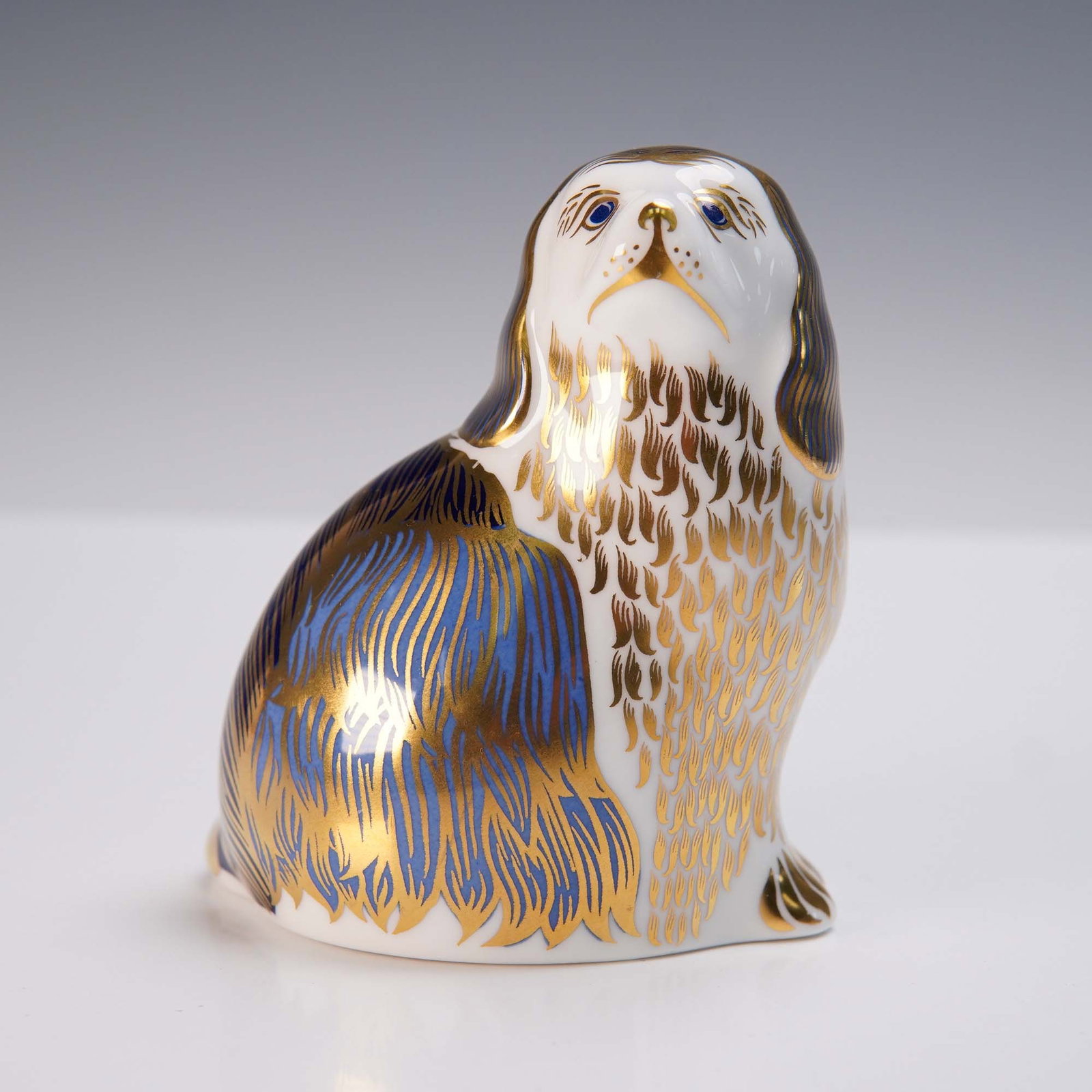 Royal Crown Derby Figurine, King Charles Spaniel: Charming English bone china figurine by Royal Crown Derby, depicting a King Charles Spaniel in a seated pose. Finely decorated with cobalt blue and 22k gold accents, the figurine showcases the brand's