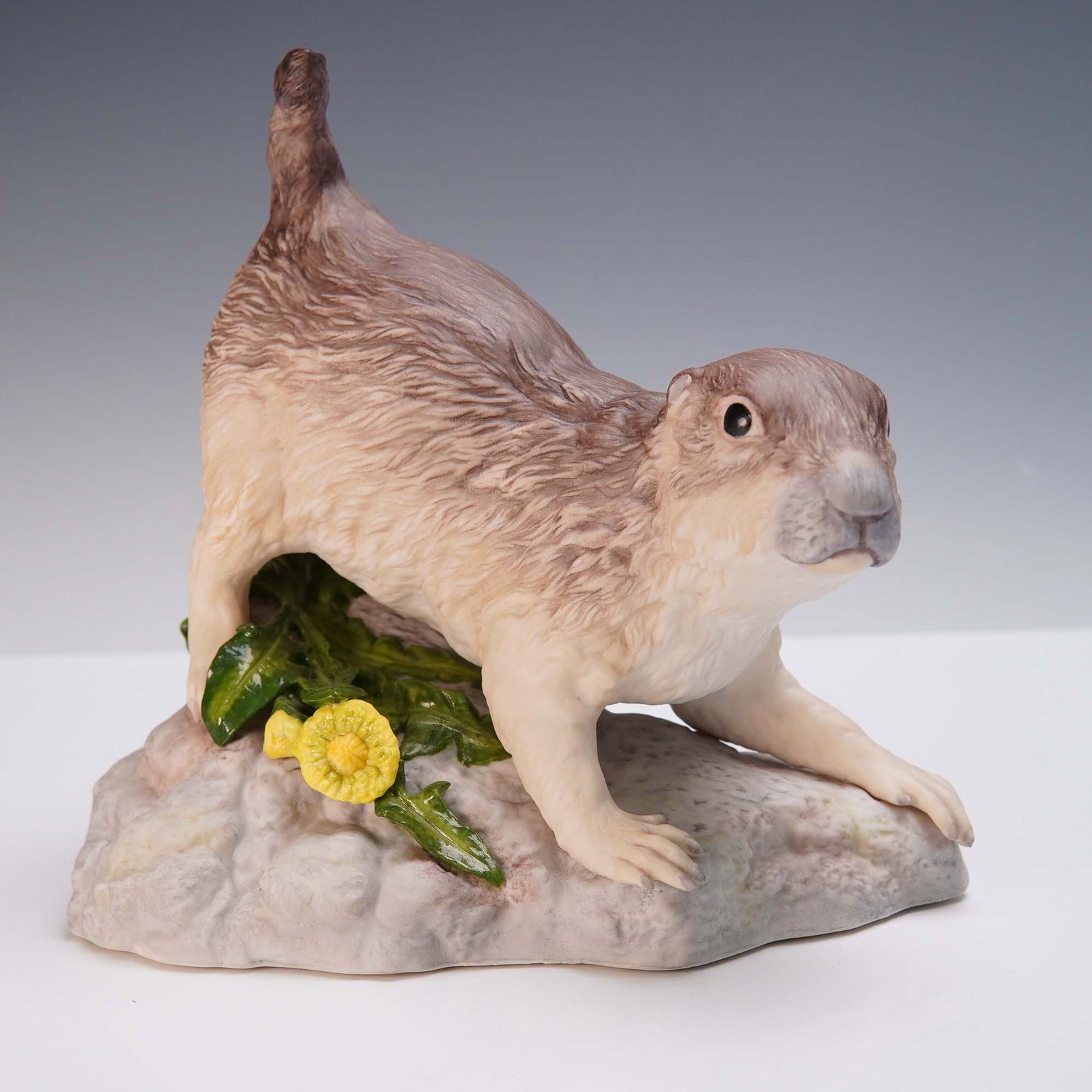Cybis Porcelain Figurine, Prairie Dog on Rocky Base: Handcrafted by Cybis Porcelain, this lifelike figurine captures the charm and alert posture of a prairie dog perched on a rocky base adorned with green foliage and a blooming yellow flower. Sculpted w