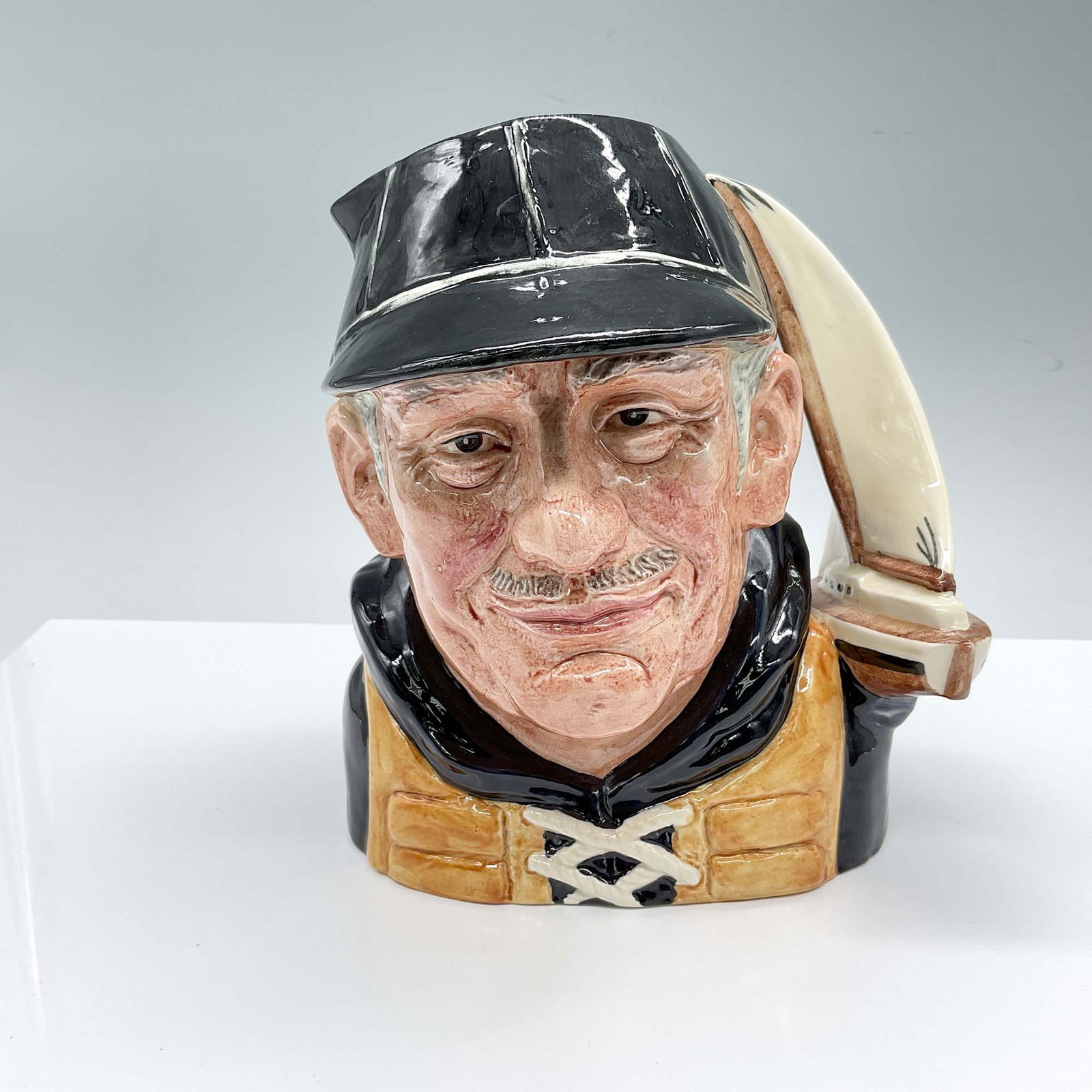 Royal Doulton Large Character Jug, Yachtsman D6622: Hand painted and hand decorated figural jug of a boatman in a black hat and yellow-orange lifejacket. The handle is shaped as a yacht with a large white sail. Royal Doulton backstamp. Artist: David B.