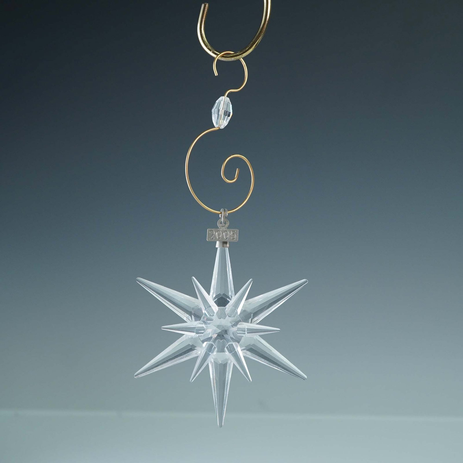 Swarovski 2005 Christmas Star Ornament with Enhancer and Box: A brilliant example of Swarovski's craftsmanship, this 2005 Christmas ornament features a striking multi-point star design in faceted clear crystal. Marked with the Swarovski swan logo and is presente