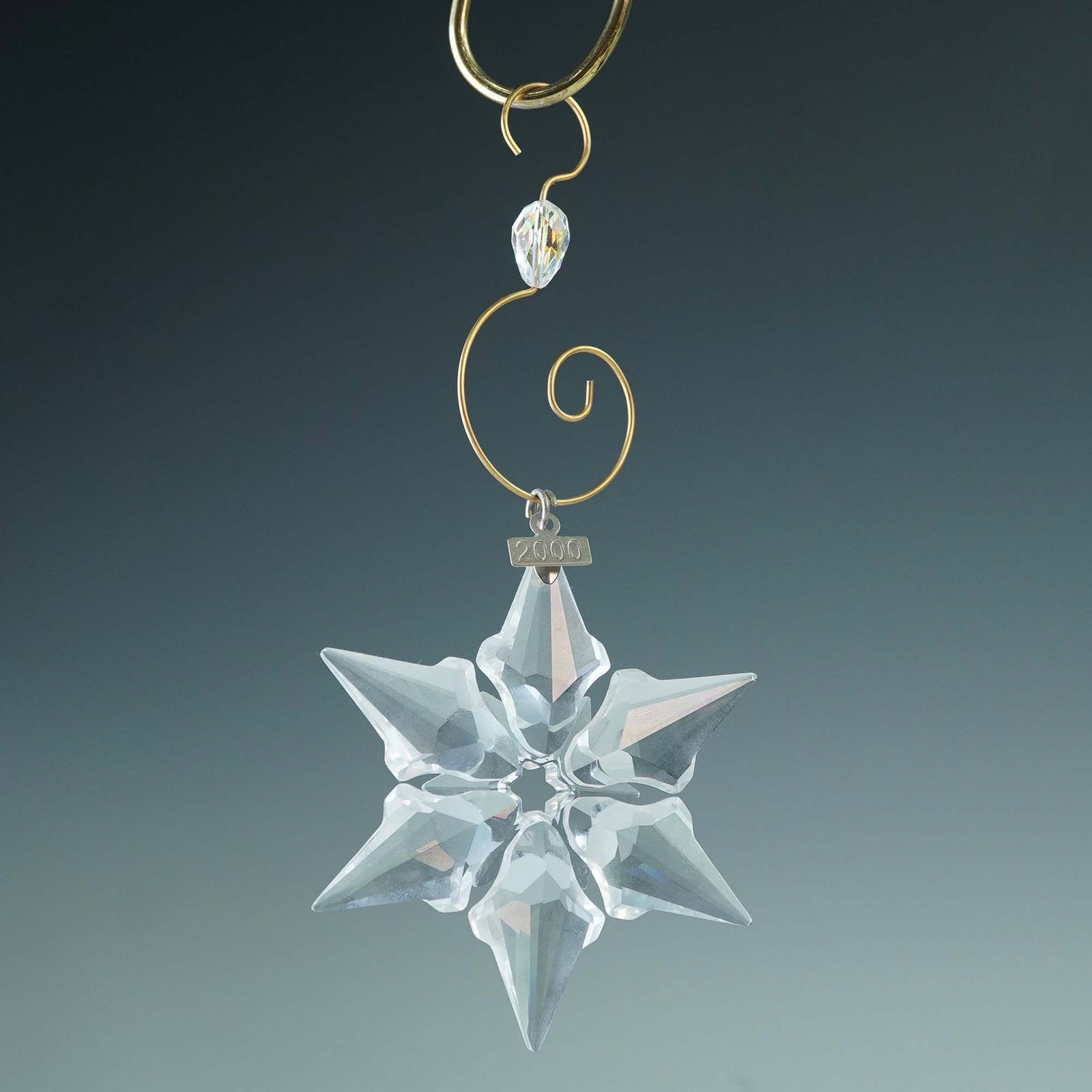 Swarovski Crystal Snowflake Ornament, 2000: This Swarovski crystal snowflake ornament from 2000 features a stunning, faceted design that captures and reflects light beautifully, creating a sparkling effect. It includes a metal year tag marked 2