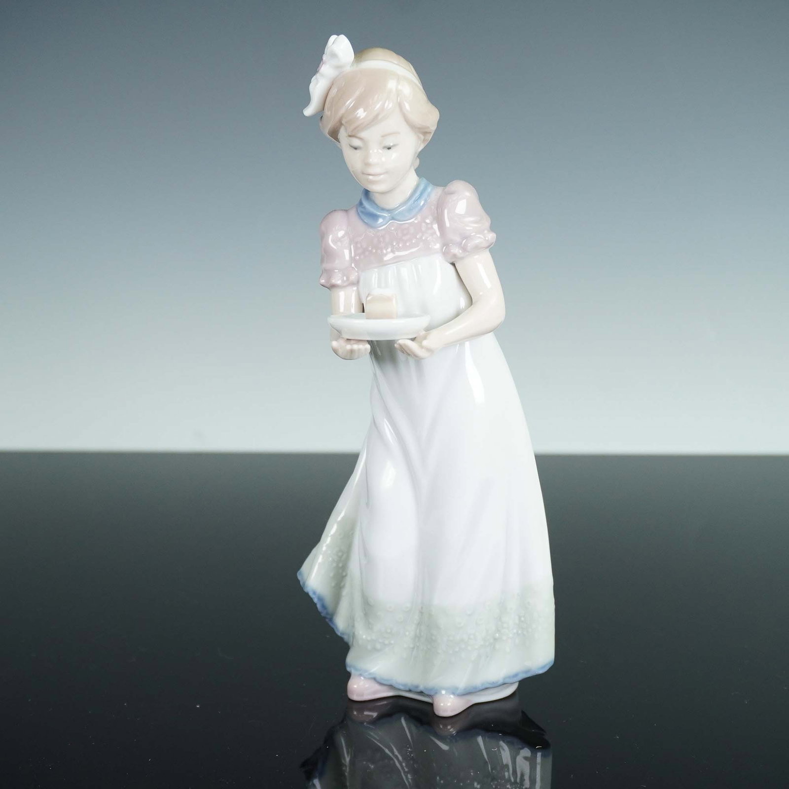 Lladro Porcelain Figurine, Happy Birthday 1005429: Lladro porcelain figurine titled Happy Birthday (model 1005429) depicts a young girl in a white gown with lavender accents, gracefully holding a plate with a small birthday cake. Crafted in Spain and 