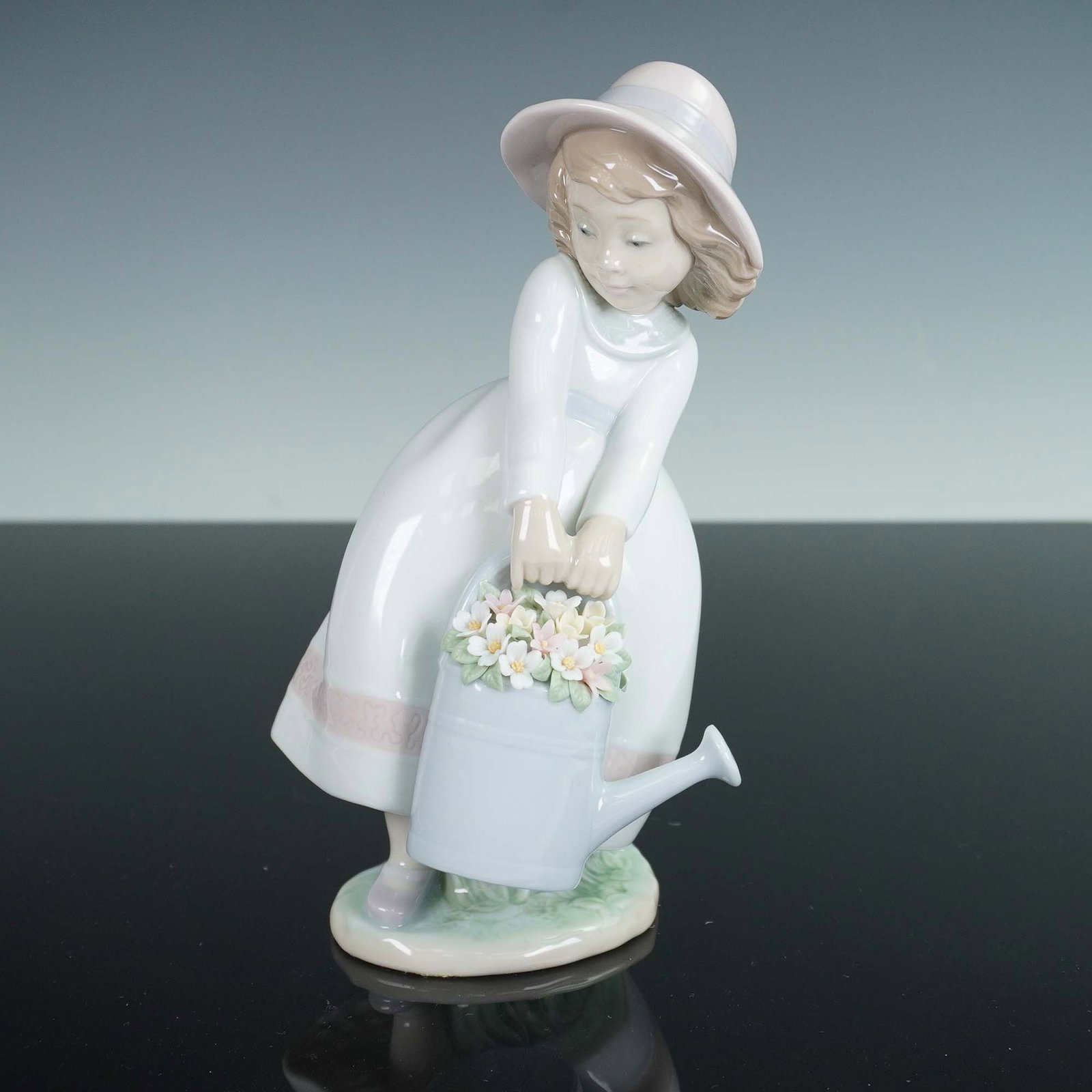 Lladro Porcelain Figurine, Springtime Fun 1006876: Lladro porcelain figurine titled Springtime Fun, number 1006876, featuring a young girl in a flowing dress and wide-brimmed hat holding a watering can brimming with pastel blossoms. This charming piec