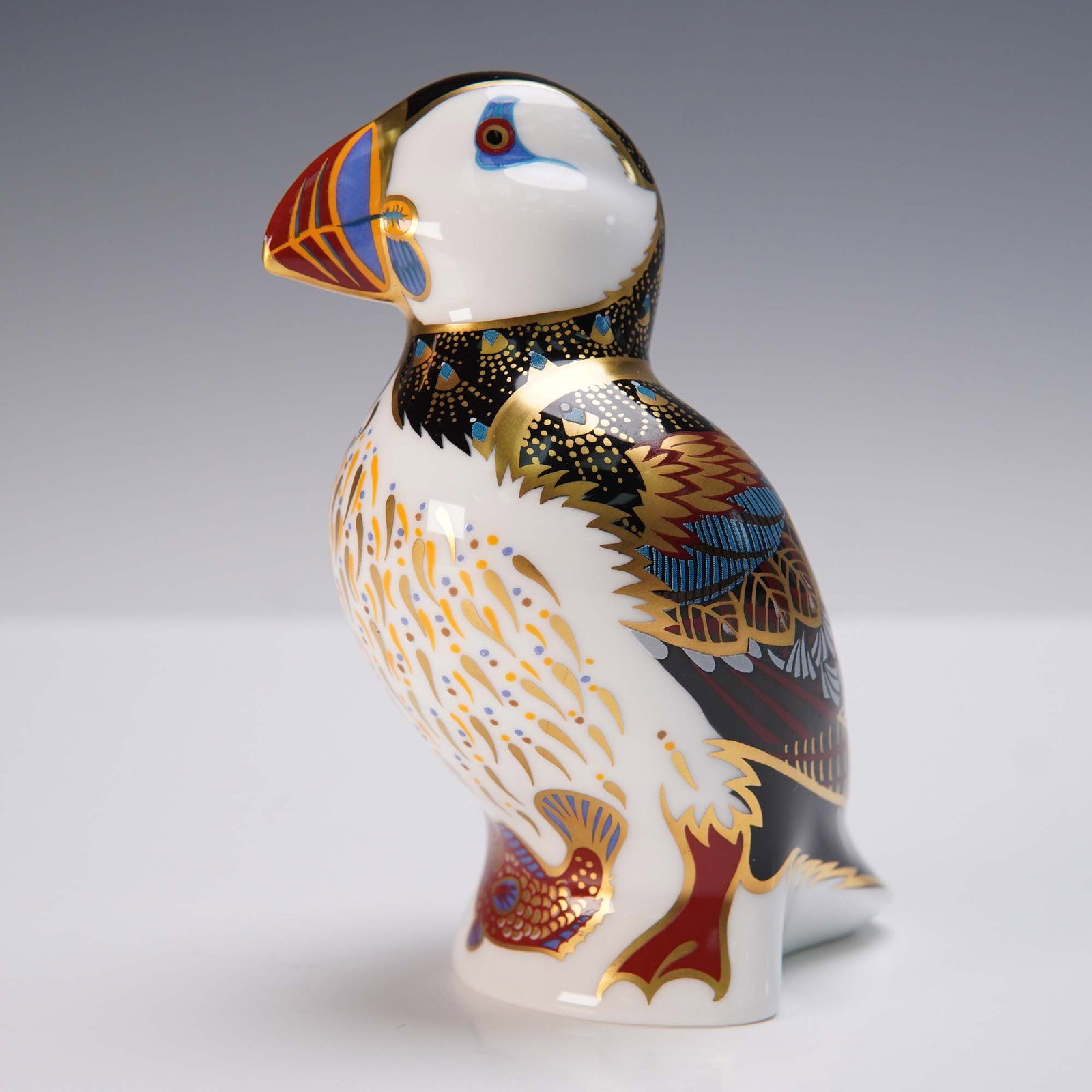 Royal Crown Derby Porcelain Puffin Paperweight LIX: This Royal Crown Derby porcelain paperweight depicts a puffin in vibrant enamels and lavish 22 karat gold accents. Crafted in England from fine bone china, the figure features a richly patterned desig