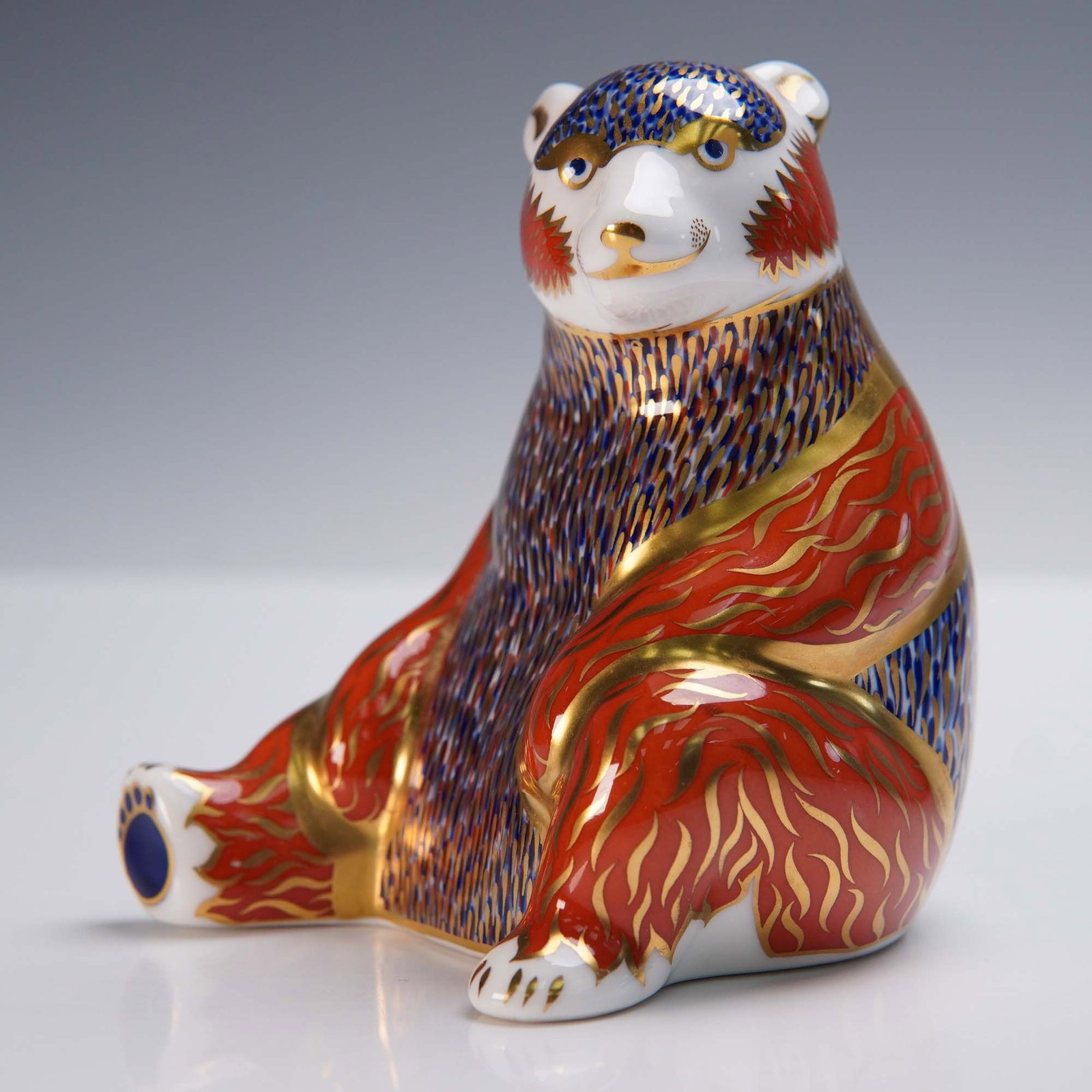 Royal Crown Derby Figurine, Honey Bear: Royal Crown Derby fine bone china figurine titled Honey Bear, decorated in warm autumnal hues with floral and gold accents. This charming bear is depicted seated with a honey jar, part of the Royal Cr