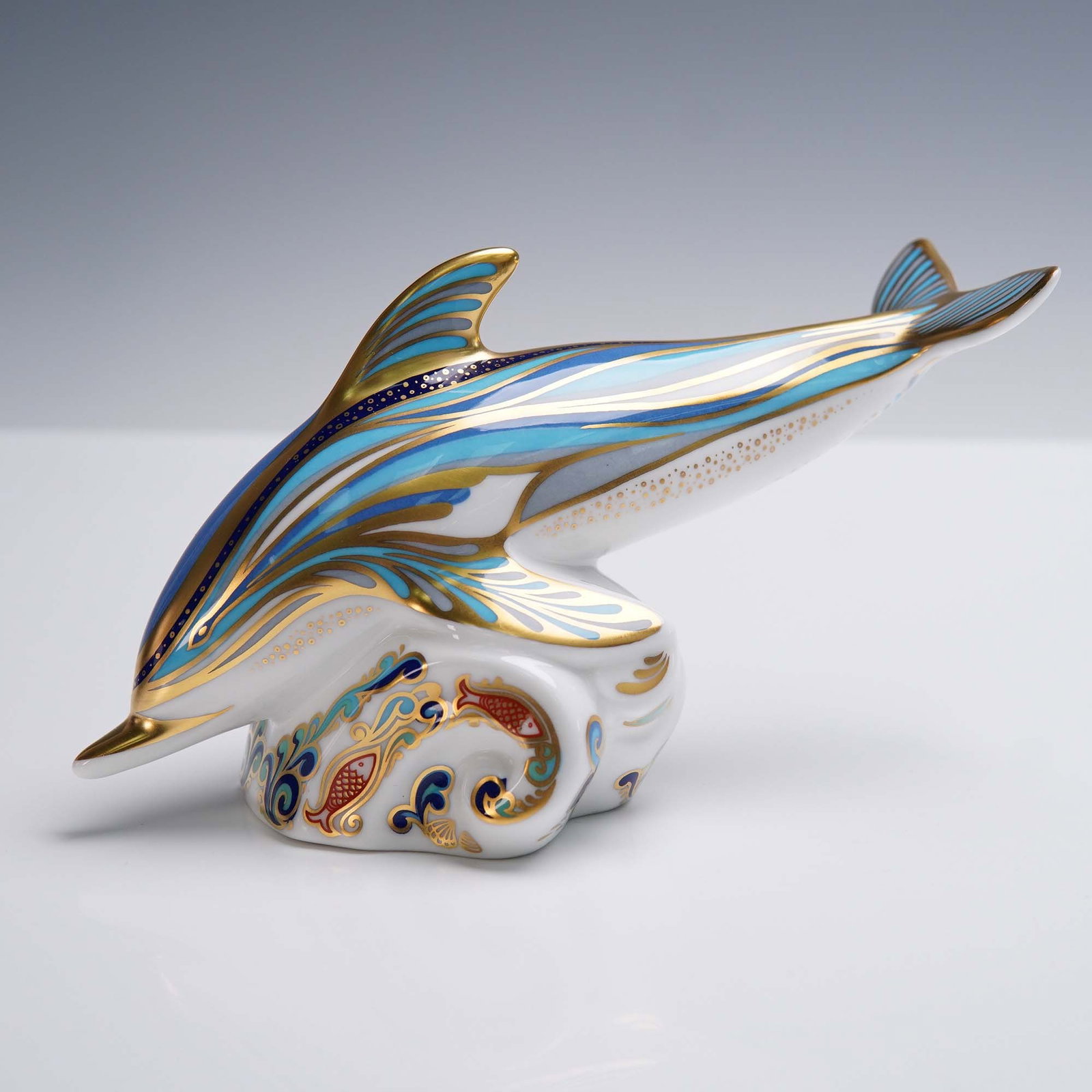 Royal Crown Derby Porcelain Paperweight, Striped Dolphin with Box: Royal Crown Derby English bone china paperweight modeled as a striped dolphin leaping over stylized ocean waves. Decorated in vibrant shades of blue, aqua, and gold, the piece features intricate patte