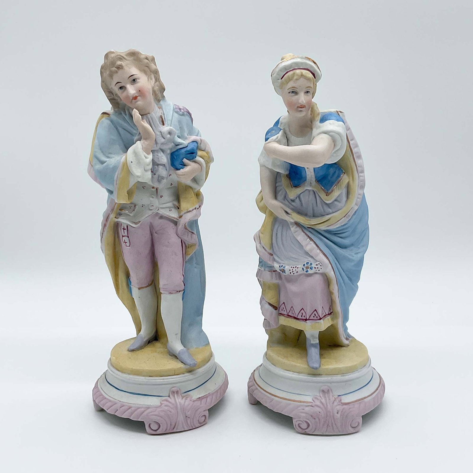 Pair of Hand-Painted Porcelain Figurines, Romantic Couple: Charming pair of hand-painted porcelain figurines featuring a romantic couple in pastel-toned attire. The male figure holds a rabbit in a tender pose, while the female figure gestures delicately, show