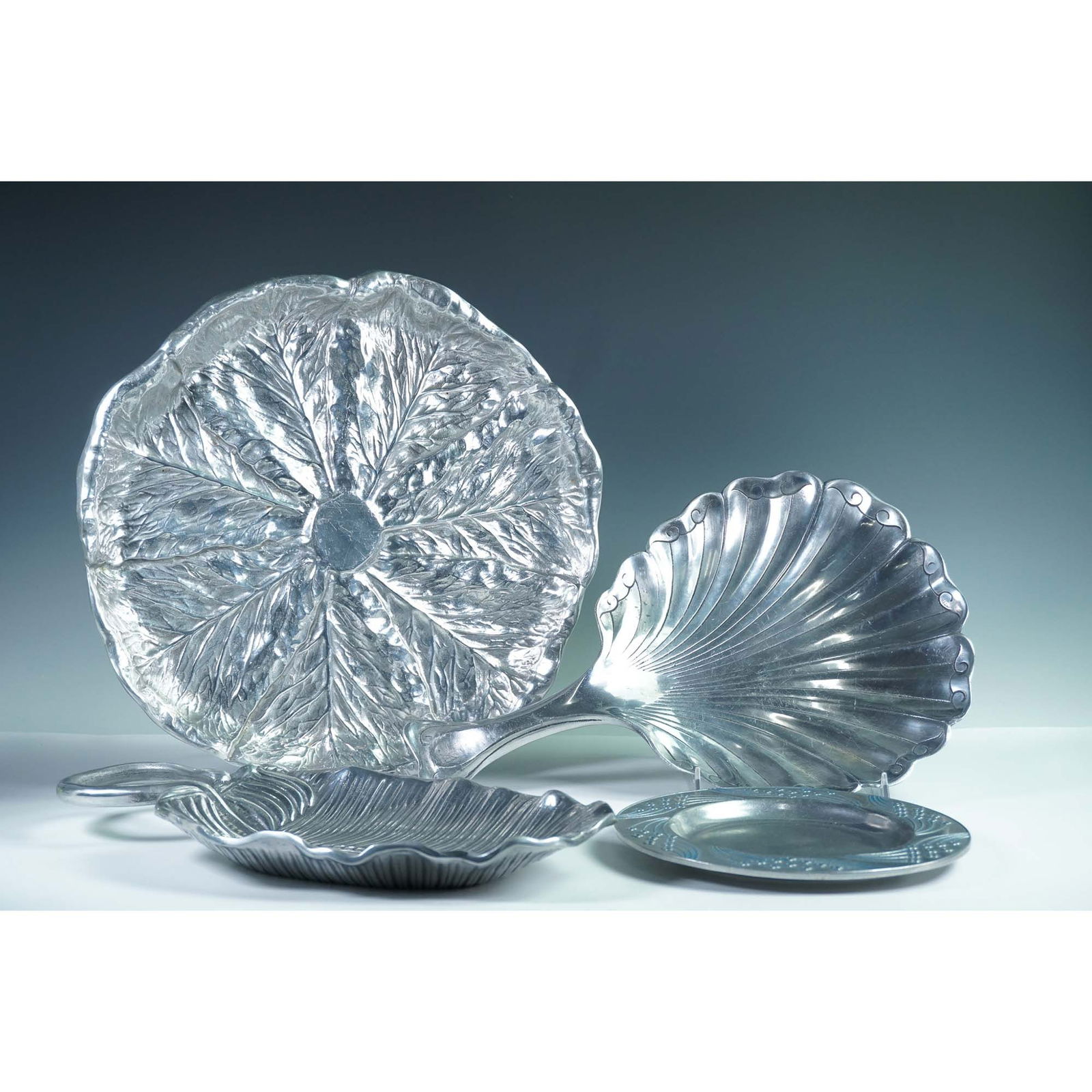 4pc Aluminum Serveware Collection, Arthur Court and Wilton: Collection of four sculptural aluminum serving trays featuring botanical and coastal motifs. Includes a large round platter marked Wilton Bruce Fox Designs with a cabbage leaf pattern; a shell-shaped