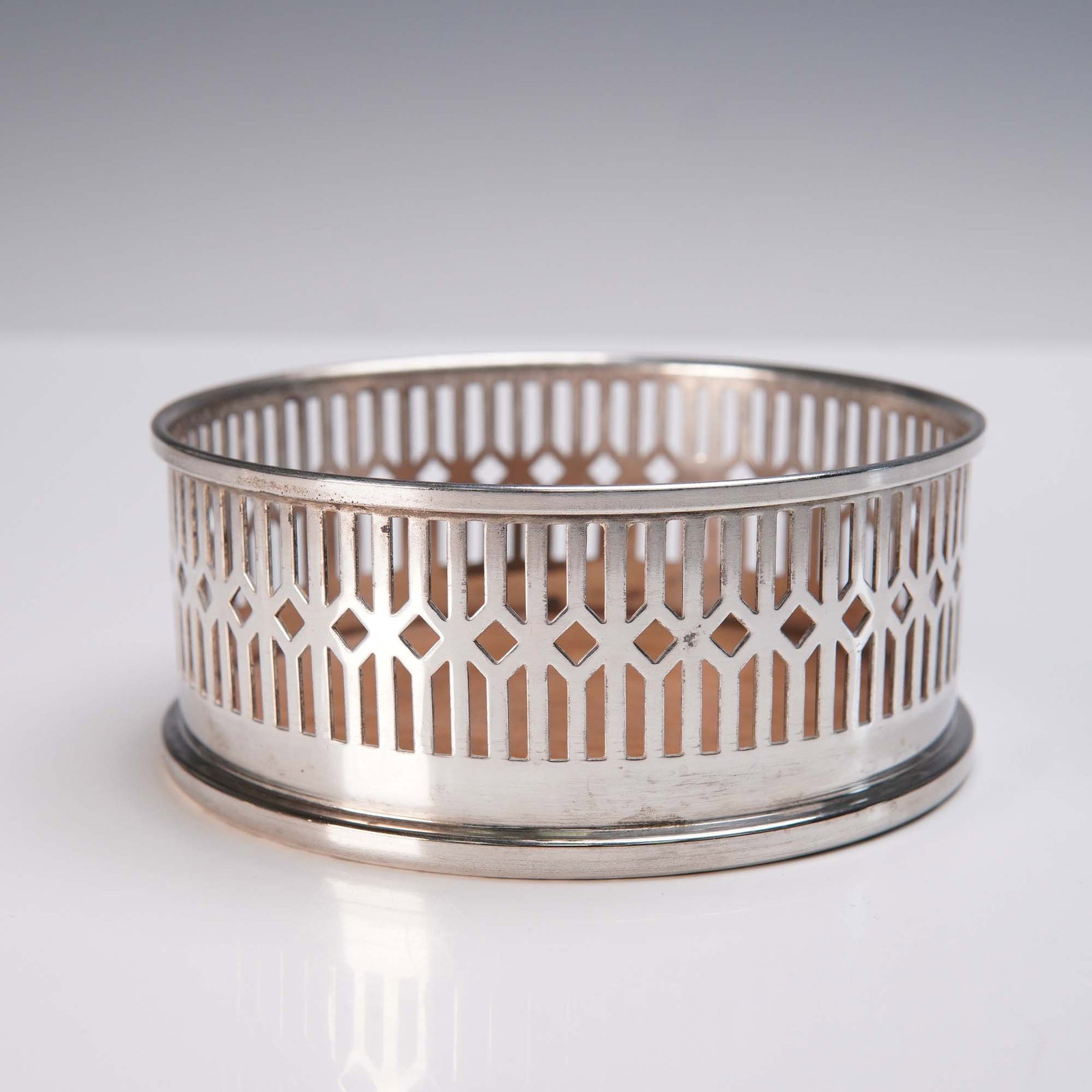 PMXX Italian Silver-Plated Wine Coaster: Features an openwork gallery-style border with geometric cutouts in a repeating diamond and vertical bar pattern. The interior base is inset with a wood disk, providing a secure resting surface for th