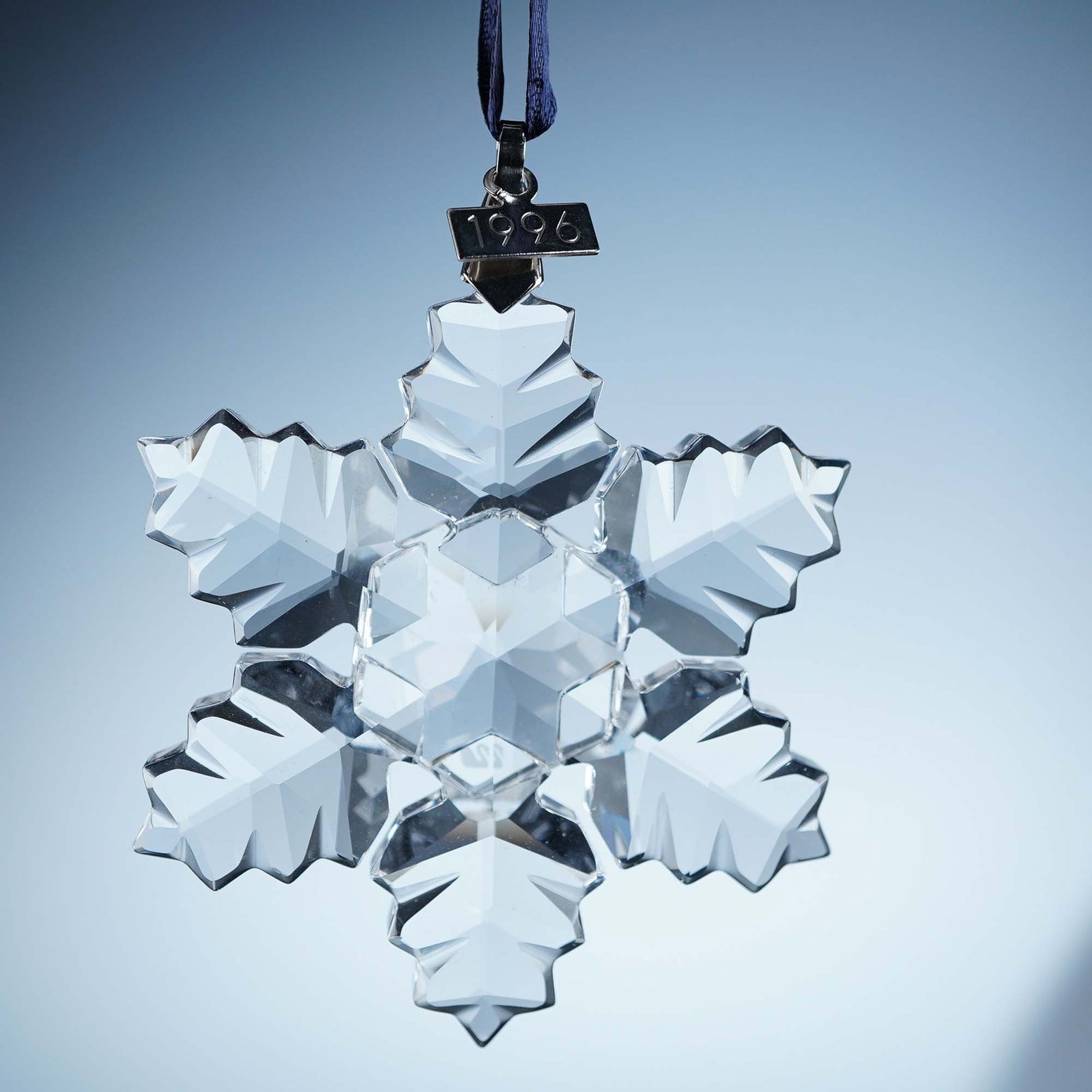 Swarovski Crystal Annual Snowflake Ornament 1996: 1996 Swarovski Crystal Annual Edition Ornament featuring a delicate six-pointed, leaf-like snowflake design crafted in precision-cut clear crystal. Suspended from a white satin ribbon, this limited-ed