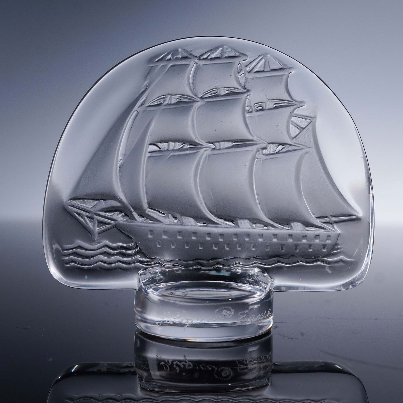 Lalique Crystal Paperweight, Caravelle: A small crystal paperweight featuring a detailed relief of a fully rigged tall ship under full sail. Executed in frosted and clear crystal, the piece displays Lalique's signature craftsmanship in capt