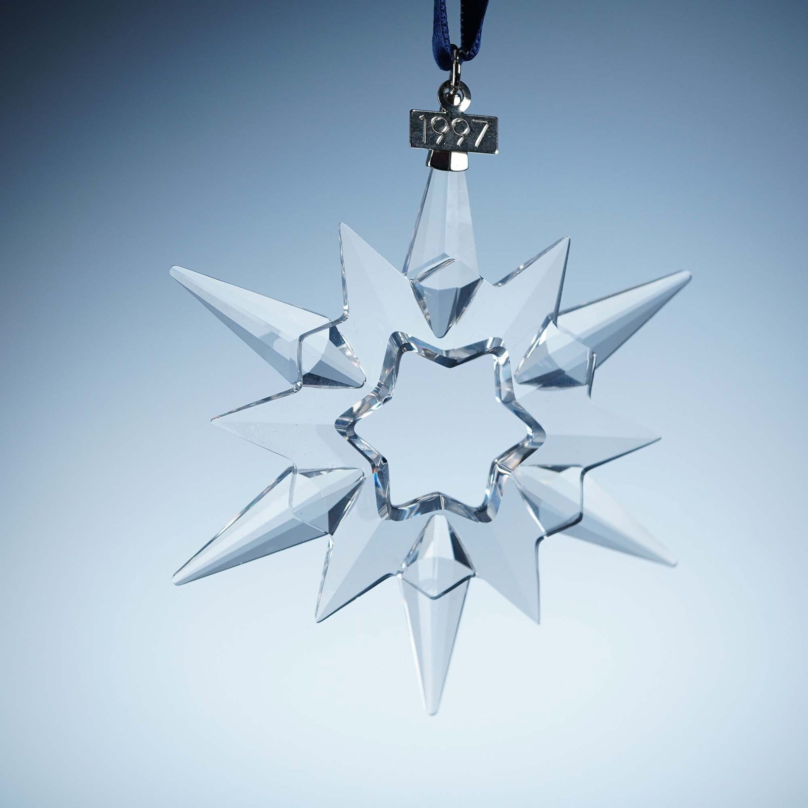 Swarovski Crystal Annual Snowflake Ornament 1997: 1997 Swarovski Crystal Annual Edition Ornament, designed in the form of a six-pointed snowflake with intricate faceted detailing. Crafted in clear crystal and suspended from a white satin ribbon, this