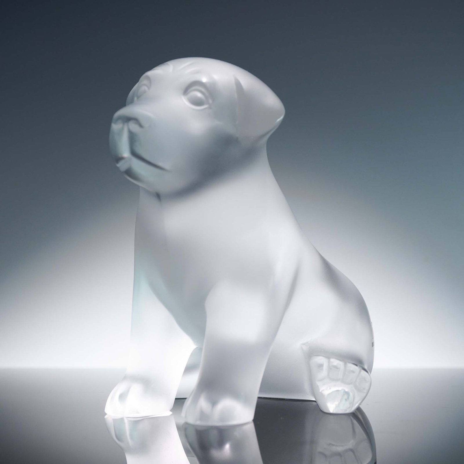 Lalique Clear Crystal Figurine, Puppy: An endearing Lalique clear crystal figurine depicting a seated puppy, crafted with a smooth frosted finish that captures the youthful innocence and playful spirit of a young dog. The expressive face a