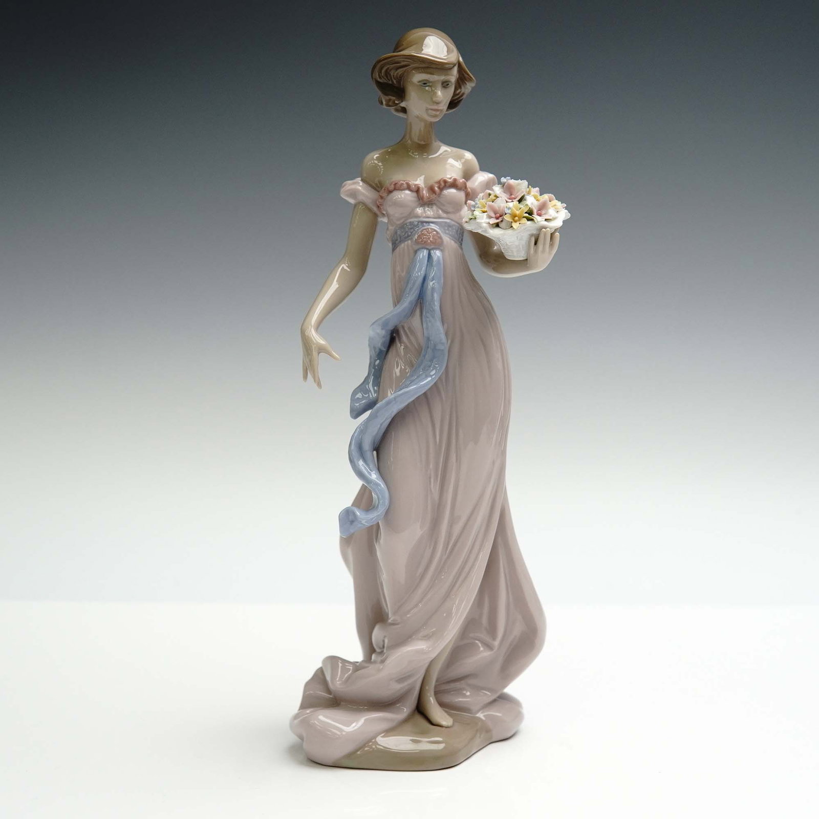 Lladro Porcelain Figurine, Spring Flirtation 01006365: Spring Flirtation (01006365) by Lladro is a romantic and charming figurine designed by Regino Torrijos and issued in 1996. The piece captures a graceful young woman strolling in a flowing gown, delica