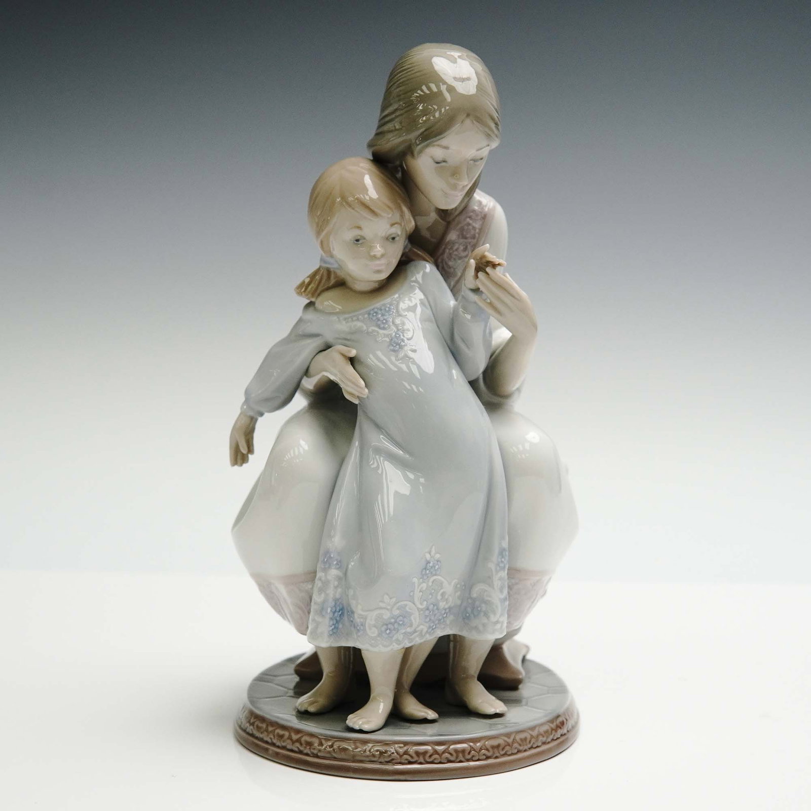 Lladro Porcelain Figurine, Tenderness 1001527: Glazed finish figure that depicts a mother tenderly holding her daughter. Lladro backstamp. Artist: Juan Huerta Issued: 1987 - 2004 Dimensions: 5.25"L x 4.25"W x 9"H Country of Origin: Spain