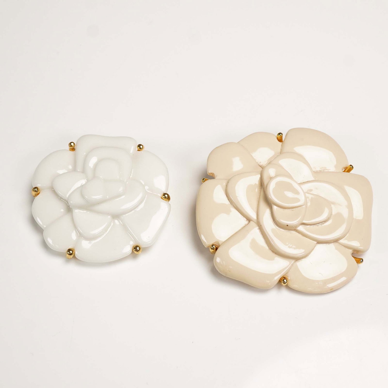 Pair of Landau White and Cream Acrylic Floral Brooches: Collection includes a white floral brooch marked Landau, designed in high-gloss acrylic with gold-tone bead accents securing each petal. Also includes a larger cream-colored floral brooch in a similar