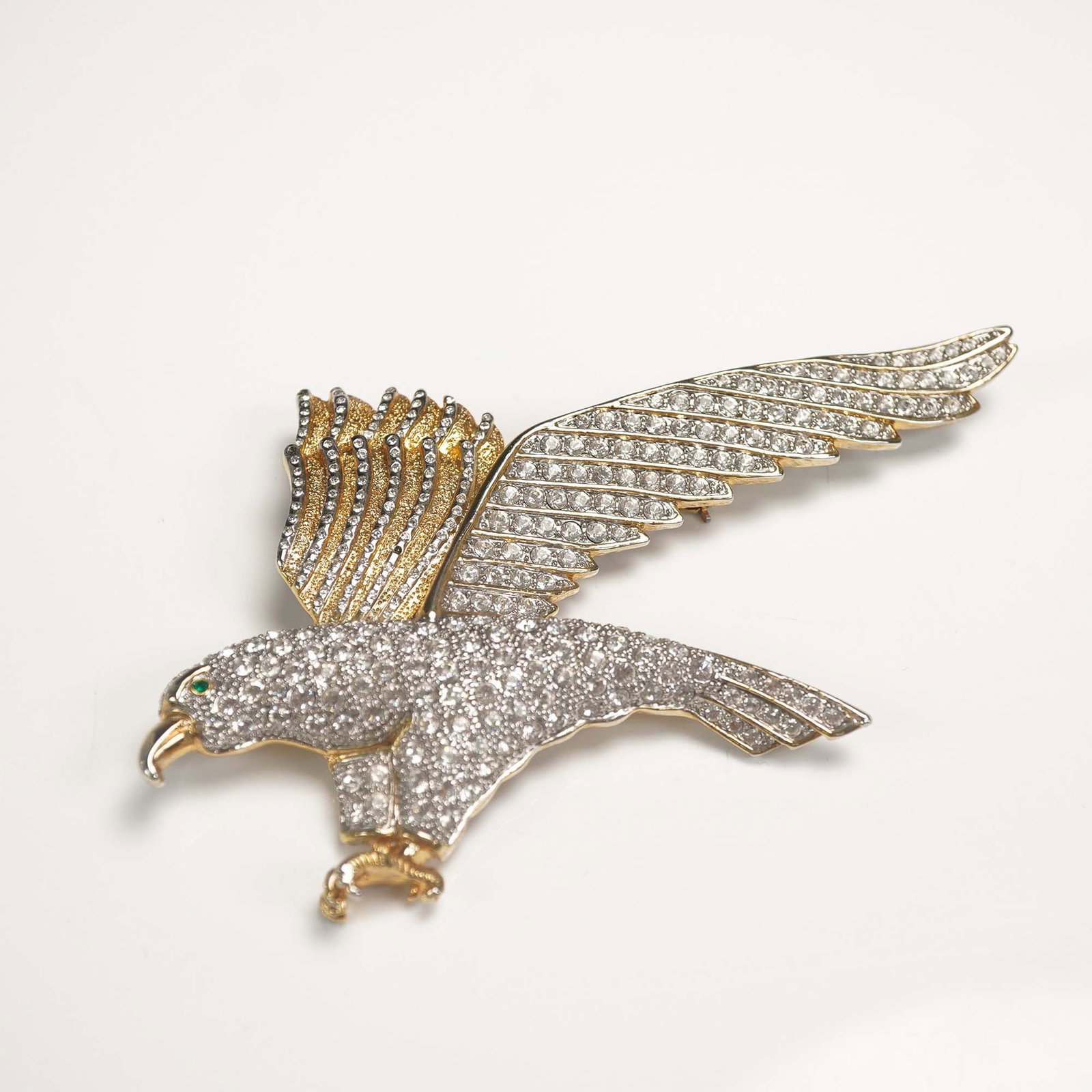 Gilded Bejeweled American Eagle Brooch: Featuring a golden eagle with outstretched wings and clutching talons, adorned with clear rhinestones across the body and wings. The eye is accented with a small green rhinestone. Reverse side include