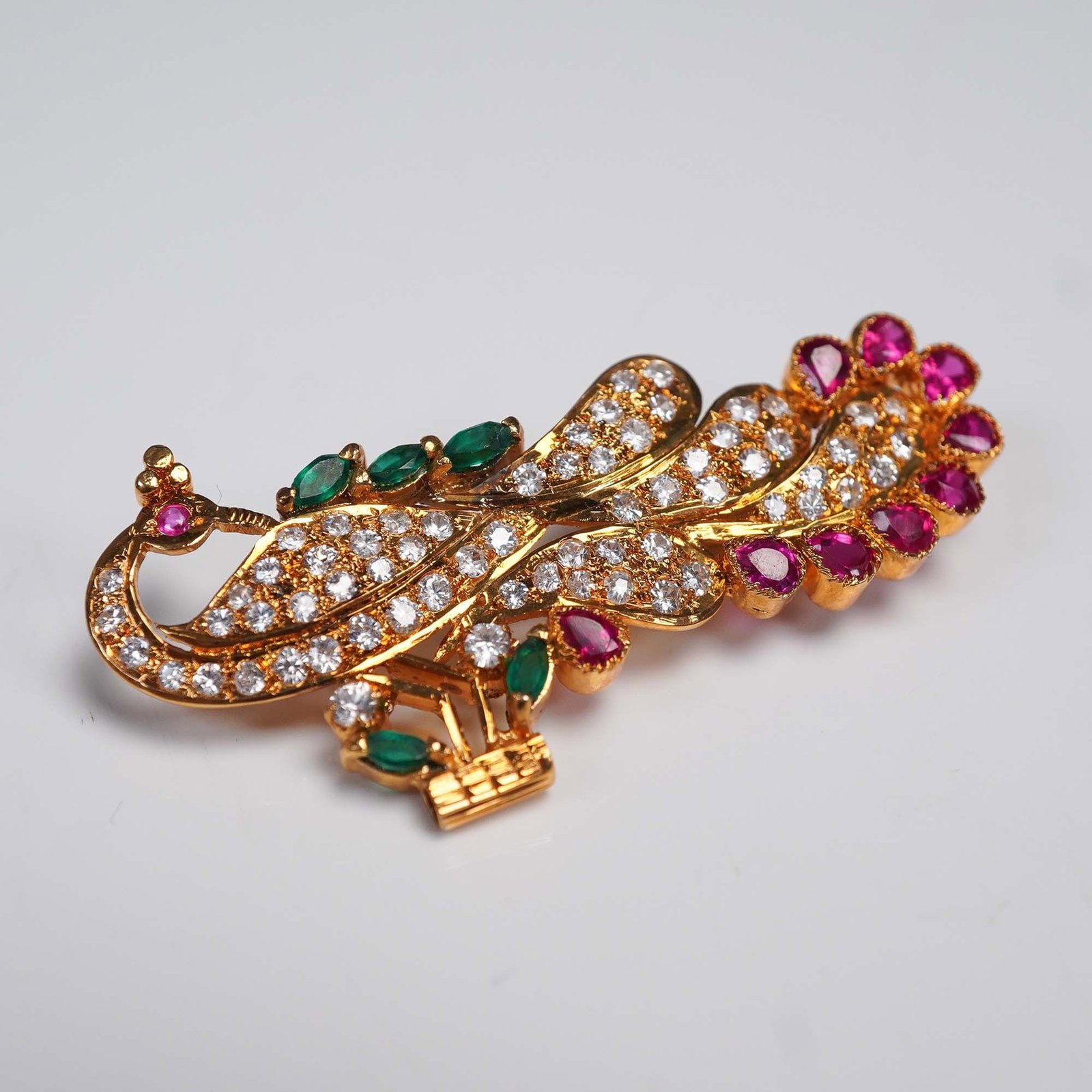 Gold Tone Peacock Brooch with Rubies and Glass Stones: This ornate gold tone brooch features an intricately designed peacock adorned with sparkling ruby stones and multicolored glass accents. The brooch showcases a sweeping tail embedded with clear round 