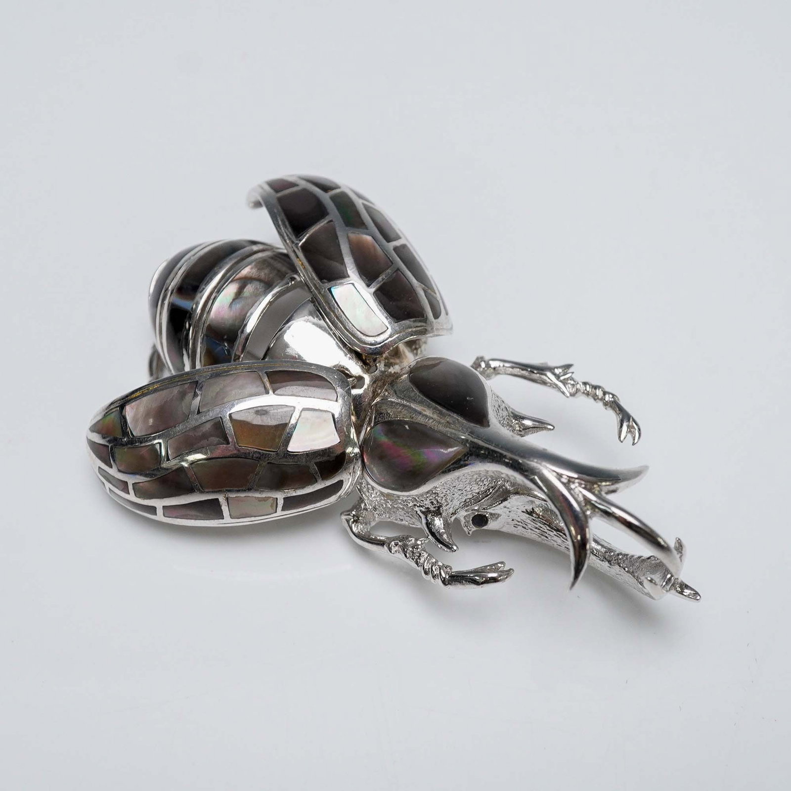 Silver-Plated Hercules Beetle Brooch: Figural brooch in the form of a Hercules beetle, crafted in silver-tone metal and detailed with curved legs, mandibles, and wing coverings. The outer carapace is inlaid with sections of dark mother of