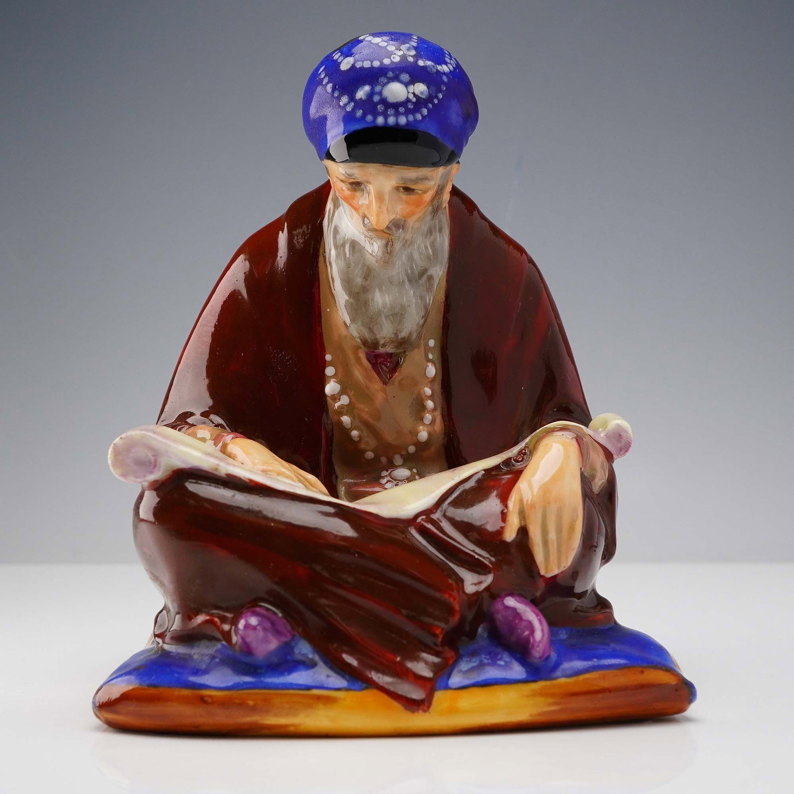 Royal Doulton Figurine, The Scribe HN1235: Hand-painted Royal Doulton figurine titled The Scribe, model HN1235, depicting a seated elderly man in rich maroon and blue robes, engrossed in reading an ancient scroll. This figure was designed by C
