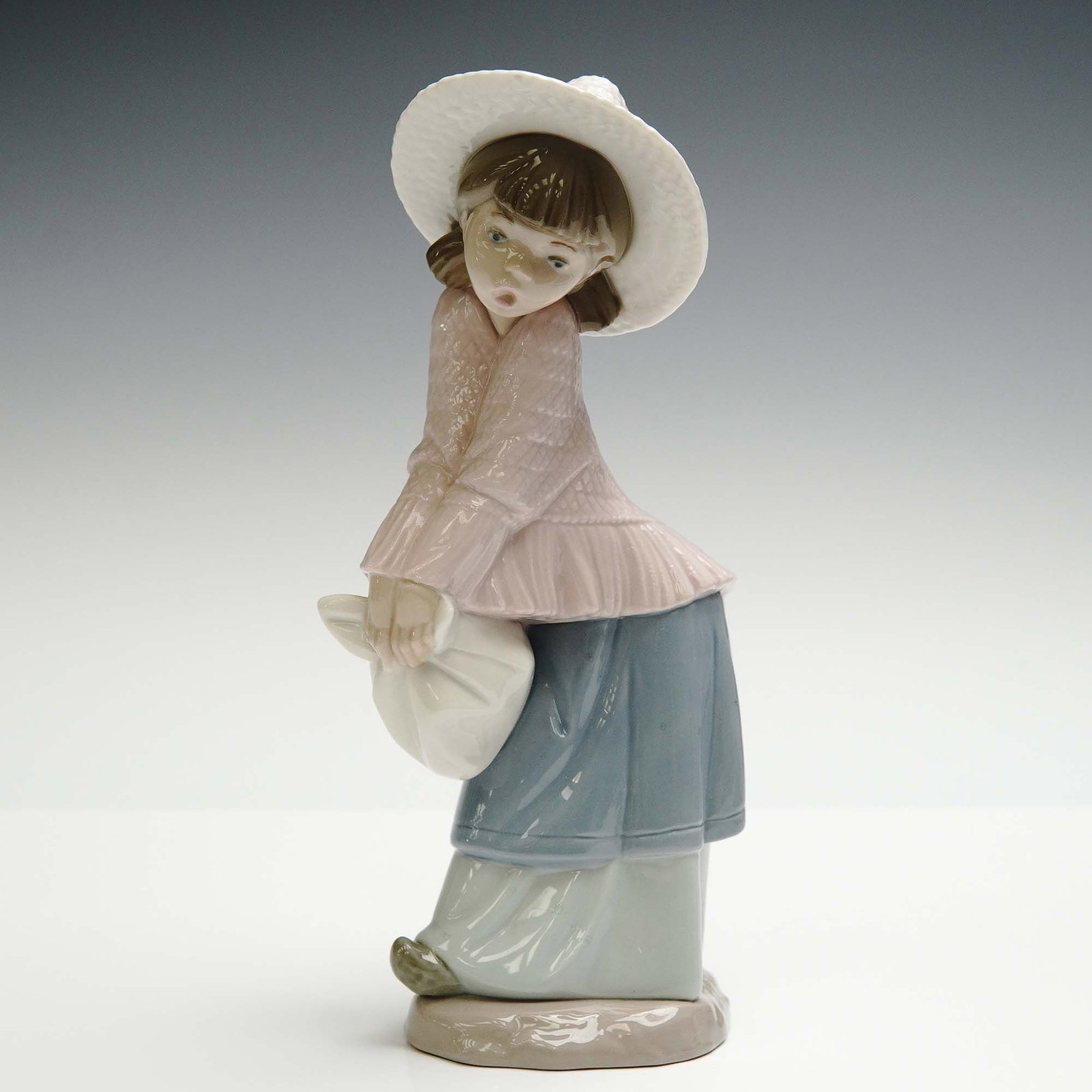Nao by Lladro Porcelain Figurine, Spanish Girl: Charming porcelain figurine by Nao, a division of the renowned Spanish maker Lladro, featuring a young girl in a pastel pink blouse and flowing blue skirt. She is portrayed with a surprised expression