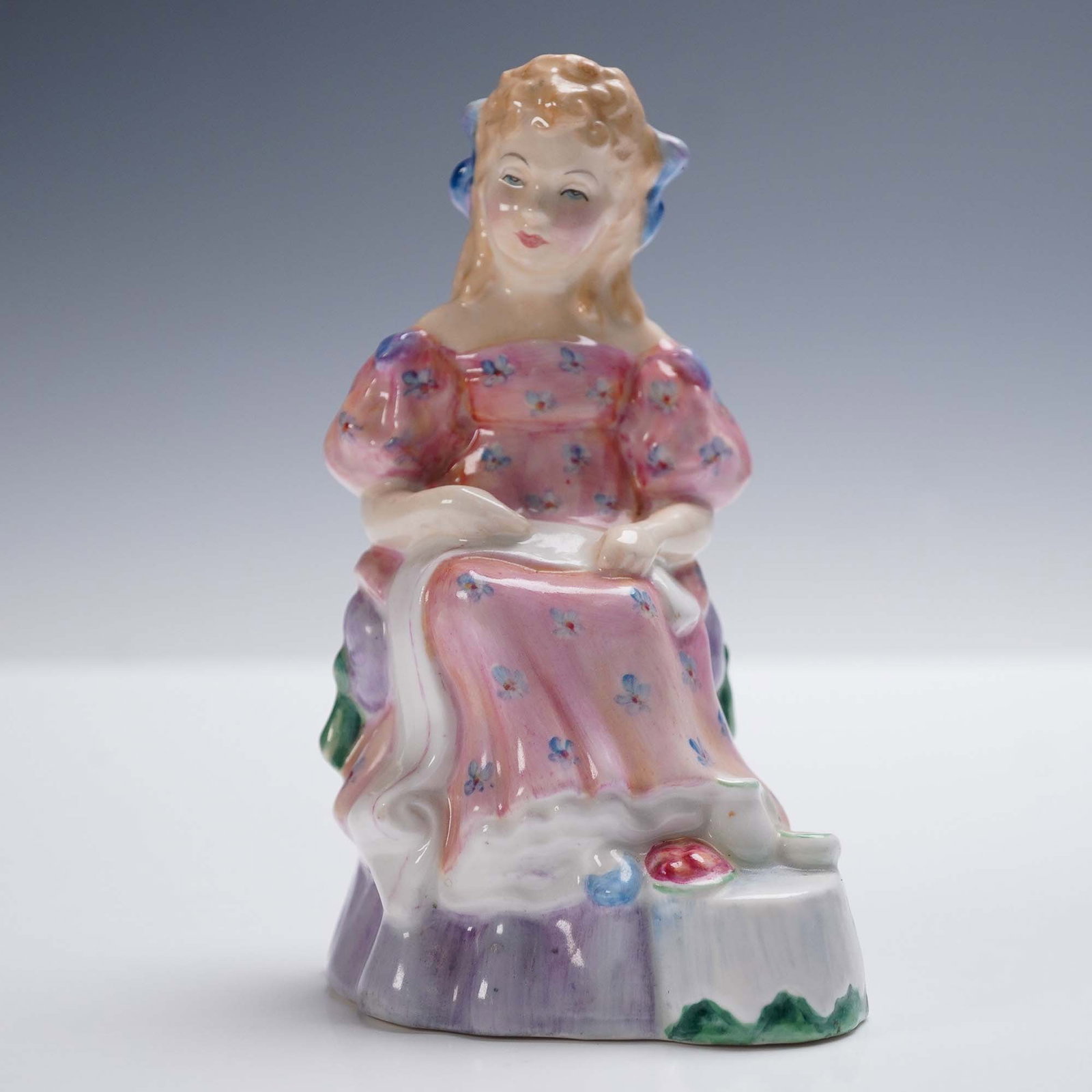 Royal Doulton Figurine, Curly Locks HN2049: This Royal Doulton porcelain figurine titled Curly Locks features a charming young girl seated with a serene expression as she engages in embroidery. She wears a flowing pink floral dress with puffed 