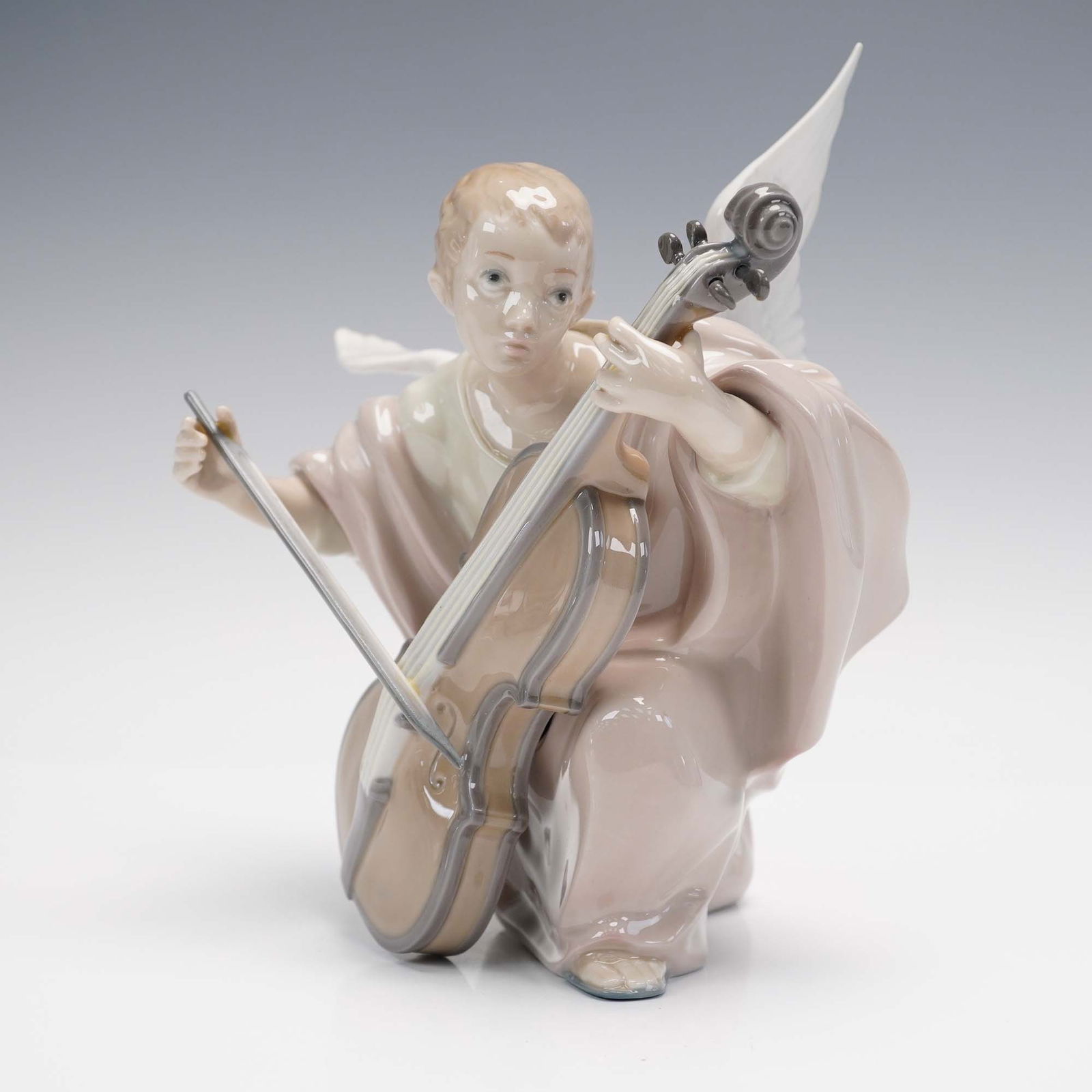 Lladro Porcelain Figurine, Heavenly Cellist #5492: Lladro's Heavenly Cellist (#01005492), sculpted by Fulgencio Garcia, depicts a serene angel in mid-performance, tenderly playing a cello with peaceful concentration. The figurine is beautifully finish