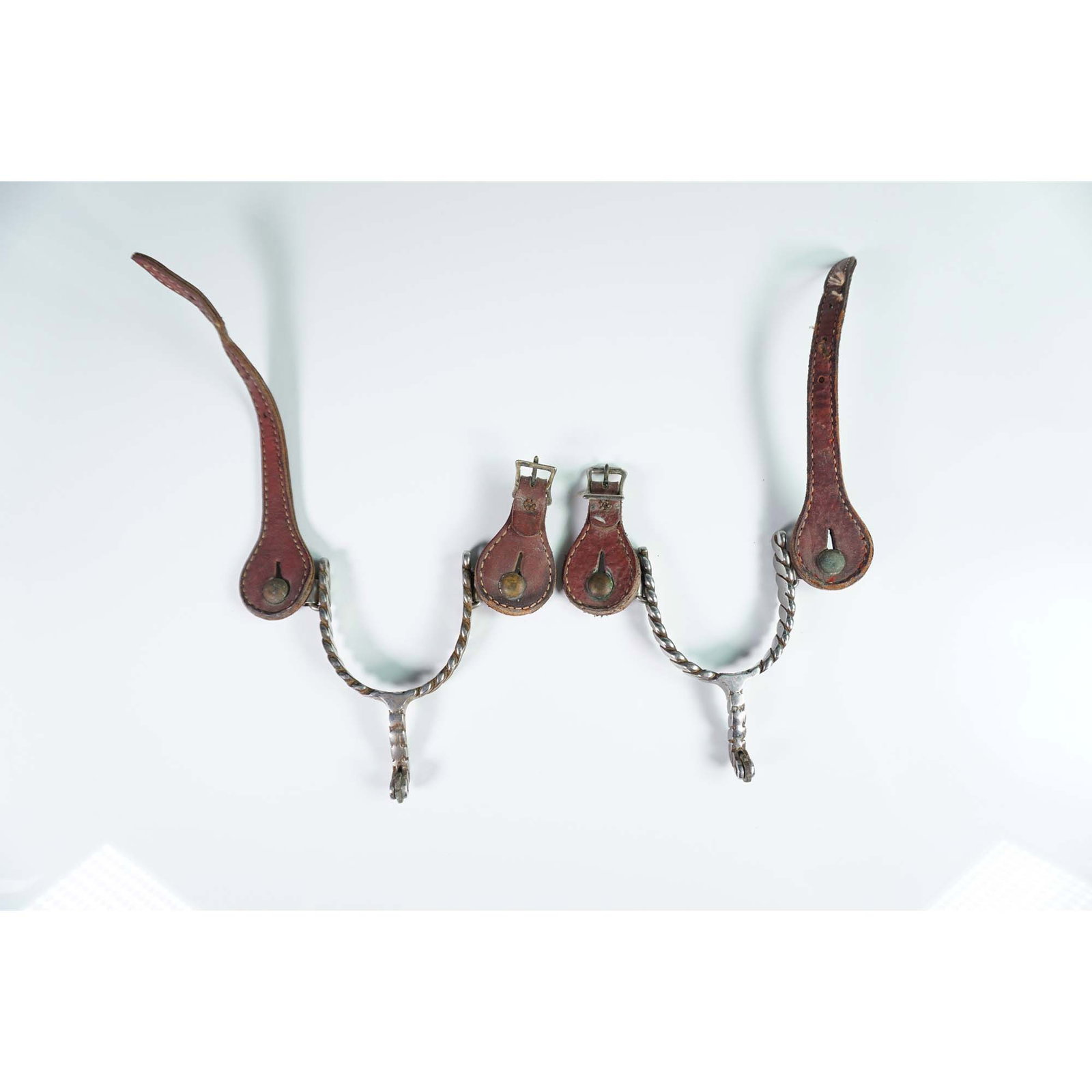 Pair of Twisted Steel Western Riding Spurs with Leather Straps: This pair of vintage Western riding spurs features twisted steel shanks and rowels, accompanied by original leather straps with stitched detailing and buckle closures. The design reflects traditional 