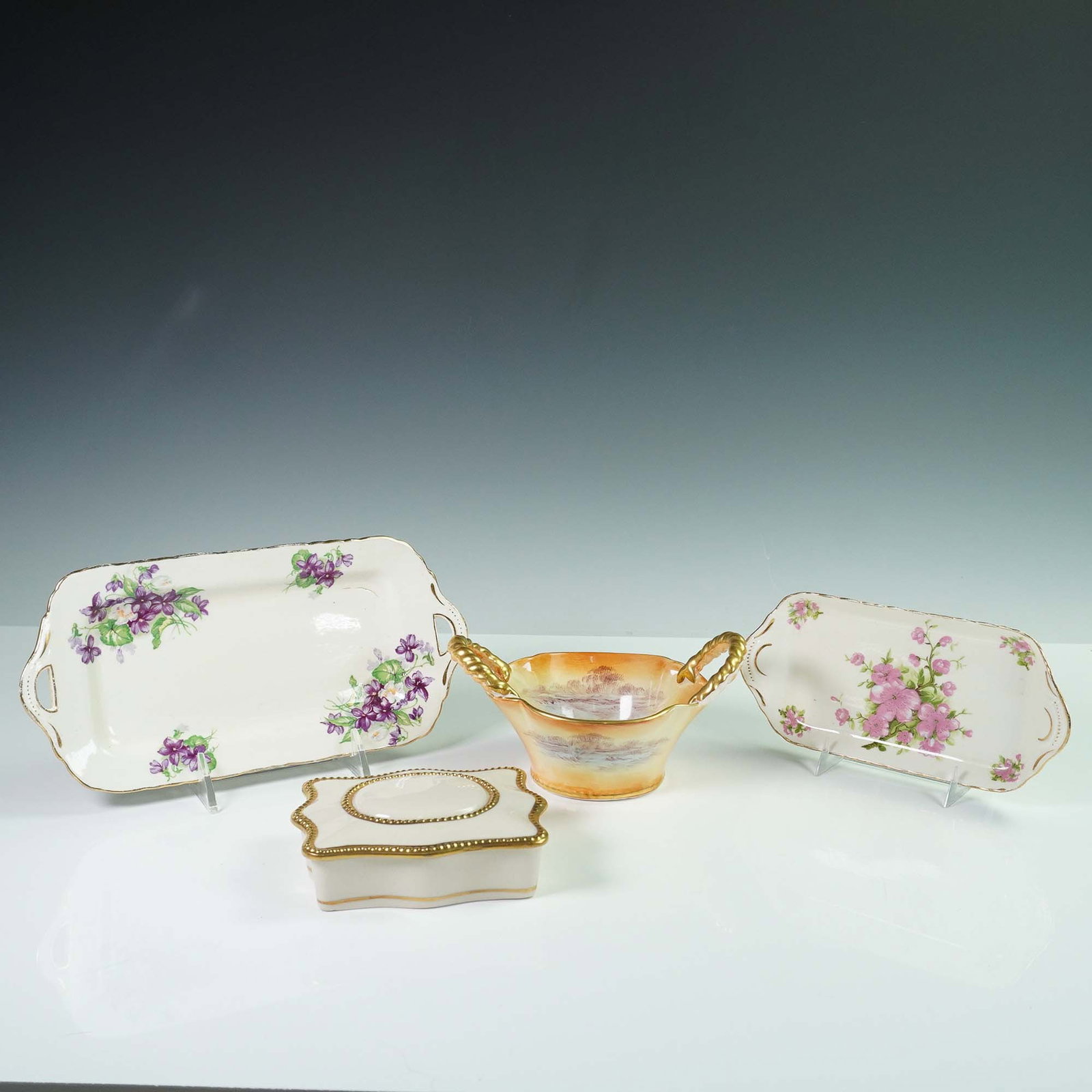 4pc Fine Bone China Grouping, H&M, Rochelle, and Crown Devon: This 4-piece fine bone china grouping includes two H&M Sutherland bone china trays, a Rochelle fine china lidded box, and a Crown Devon "Devon Glory" handled basket. The largest piece, one of the H&M 