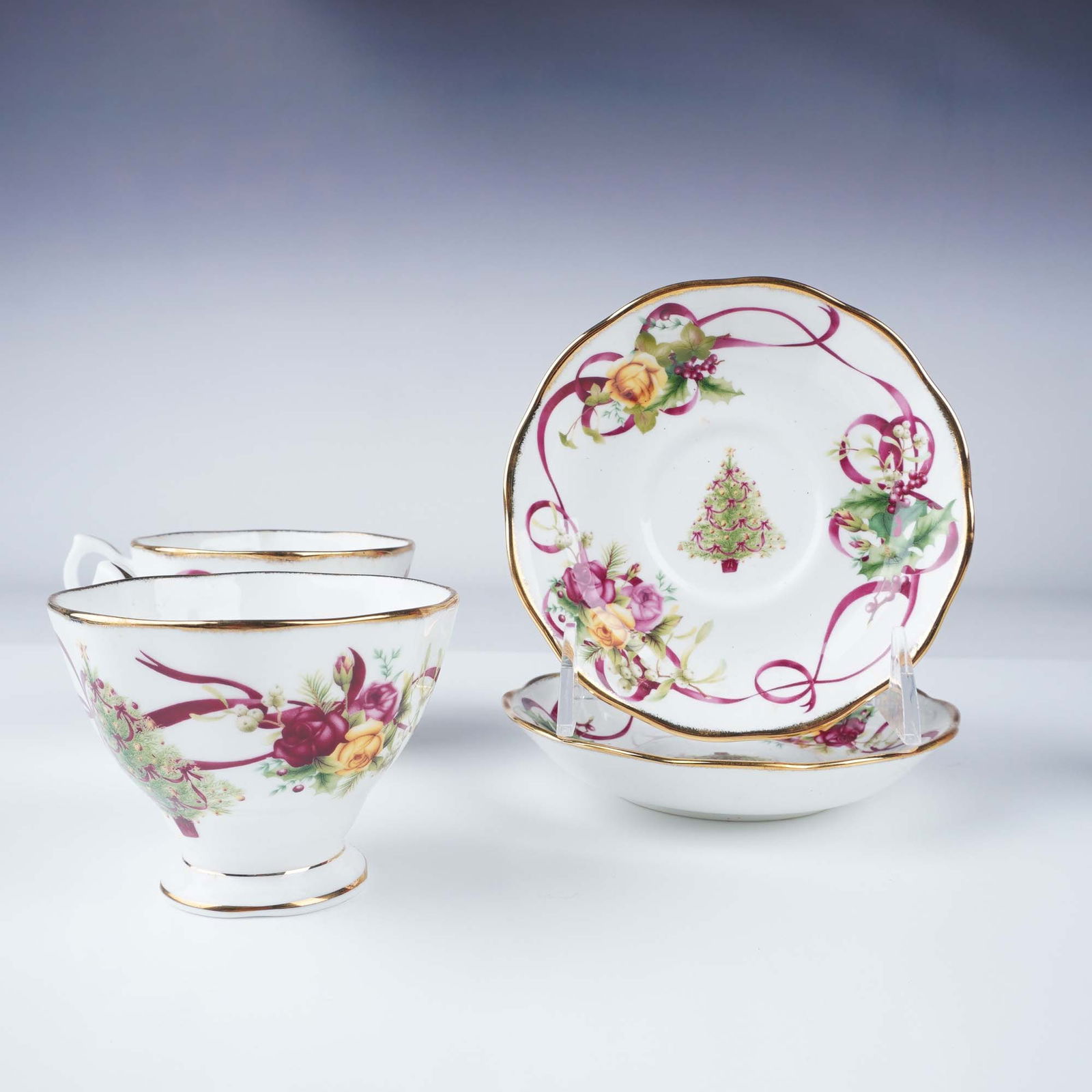 Set for 2 Royal Albert Cup and Saucer Set, Christmas Tree Motif: Royal Albert 4-piece bone china cup and saucer set featuring a festive Christmas-themed design with floral accents, ribbons, and a decorated Christmas tree motif. Each cup and saucer is adorned with e