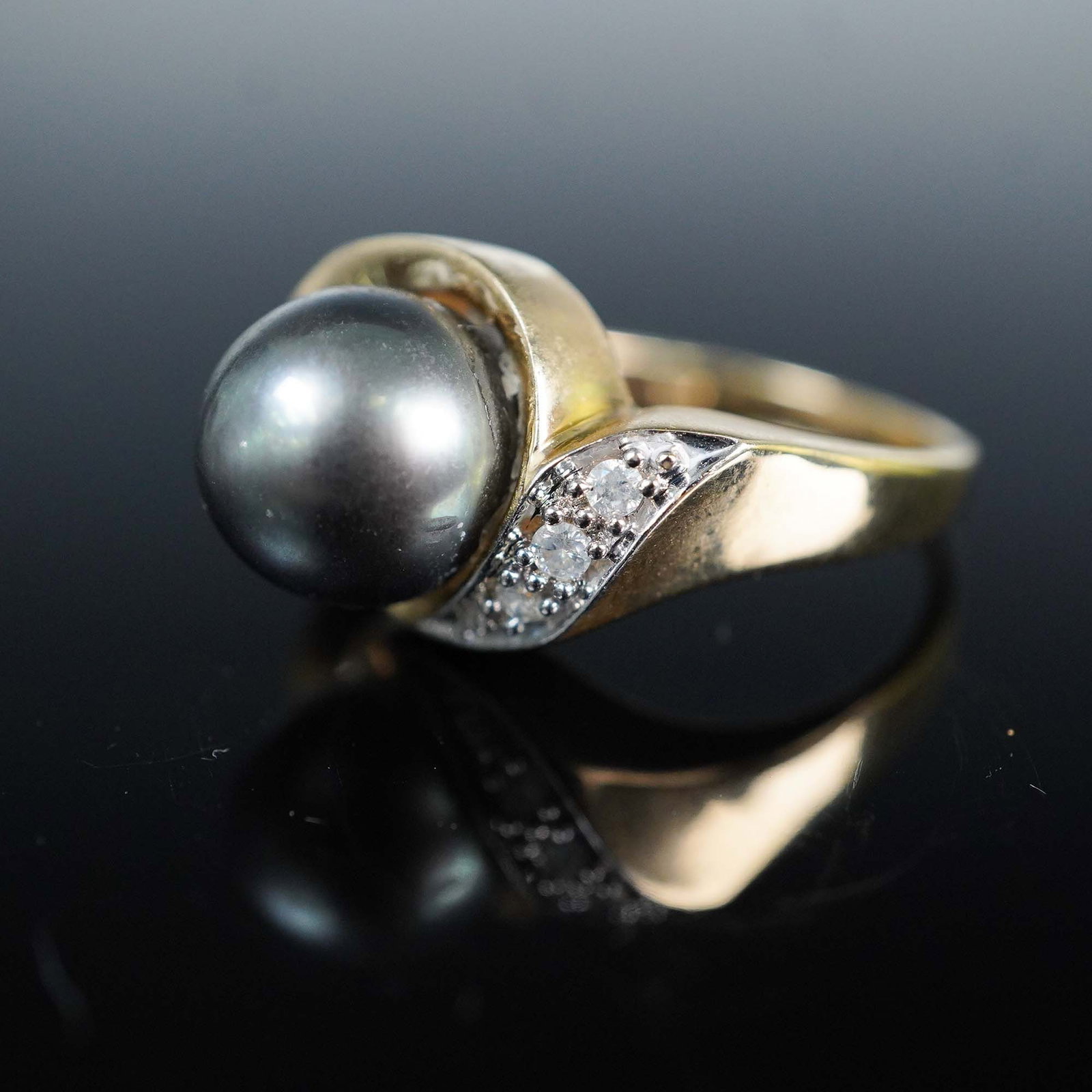 Gold Diamond and Pearl Ring: This 14kt gold ring features a 9.38mm Tahitian black pearl as its centerpiece, known for its rich luster and natural dark hue. Accenting the pearl are three round brilliant-cut diamonds, adding subtle