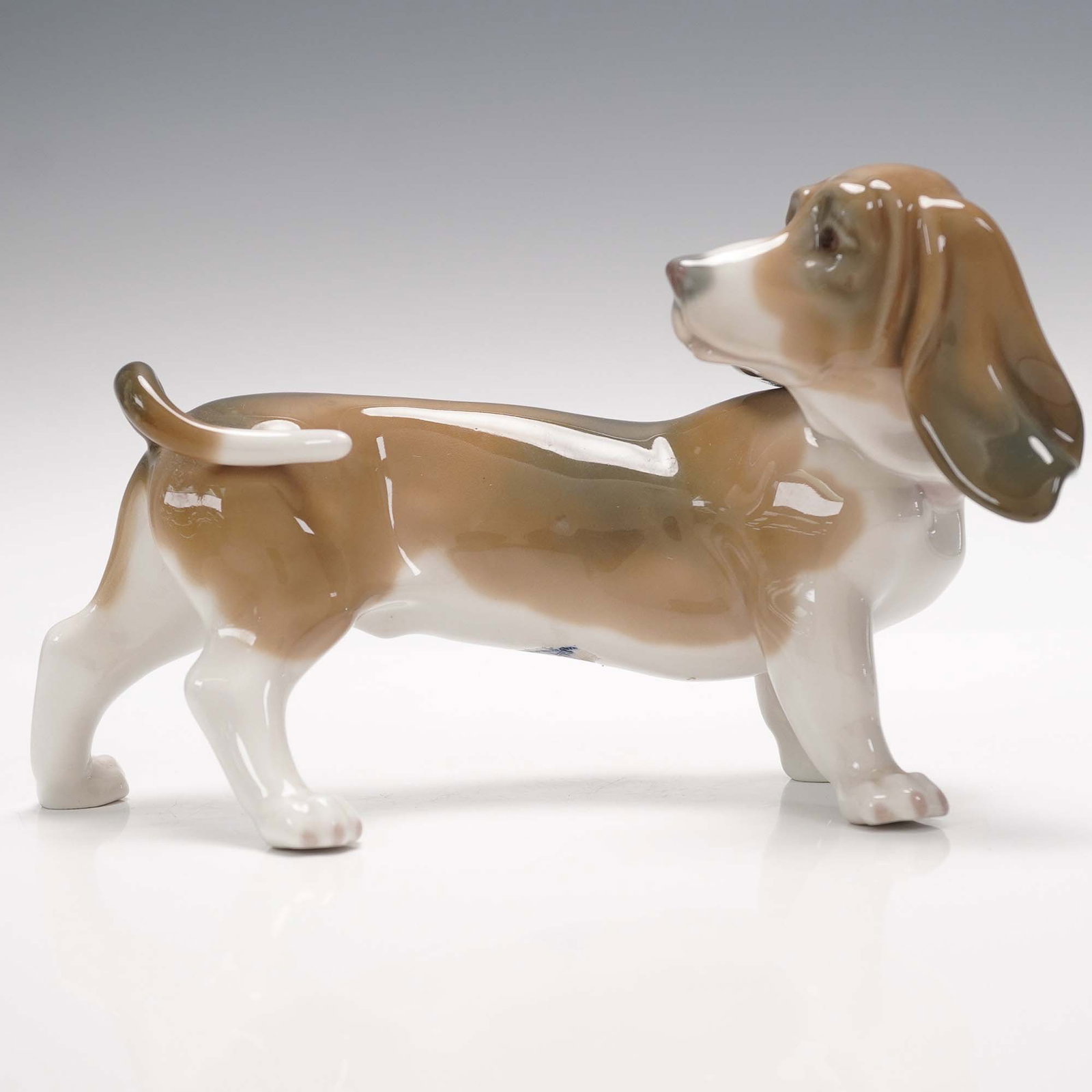 Lladro Porcelain Figurine, Basset Hound: Handcrafted by Lladro, the renowned Spanish porcelain house known for its delicate artistry and expressive sculpting, this charming figurine captures a basset hound in a lifelike pose. Sculpted by Vic