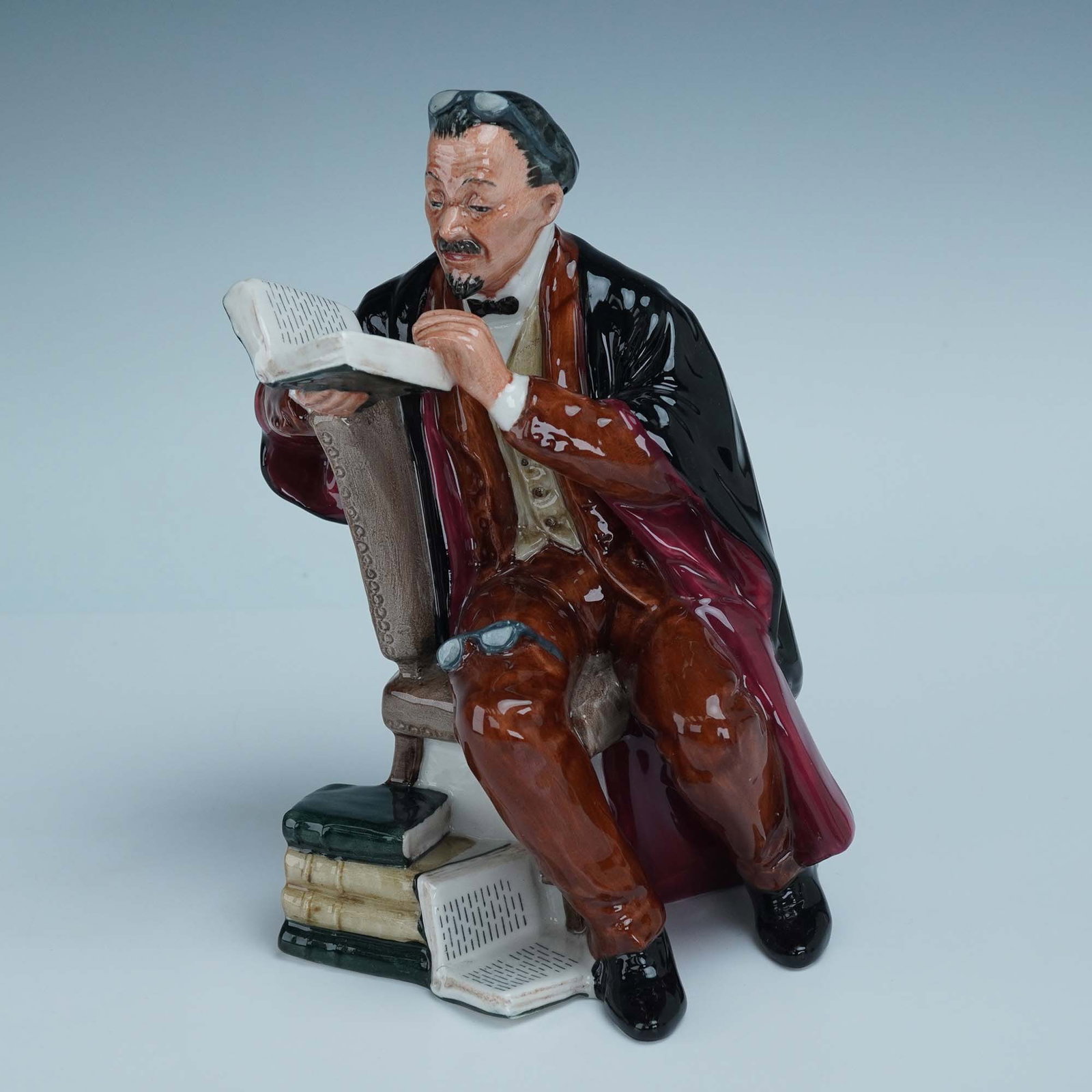 Royal Doulton Figurine, The Professor HN2281: Royal Doulton porcelain figurine titled The Professor, model HN2281. This hand-painted figure depicts a scholarly gentleman deeply engrossed in a book, seated beside a stack of volumes with spectacles