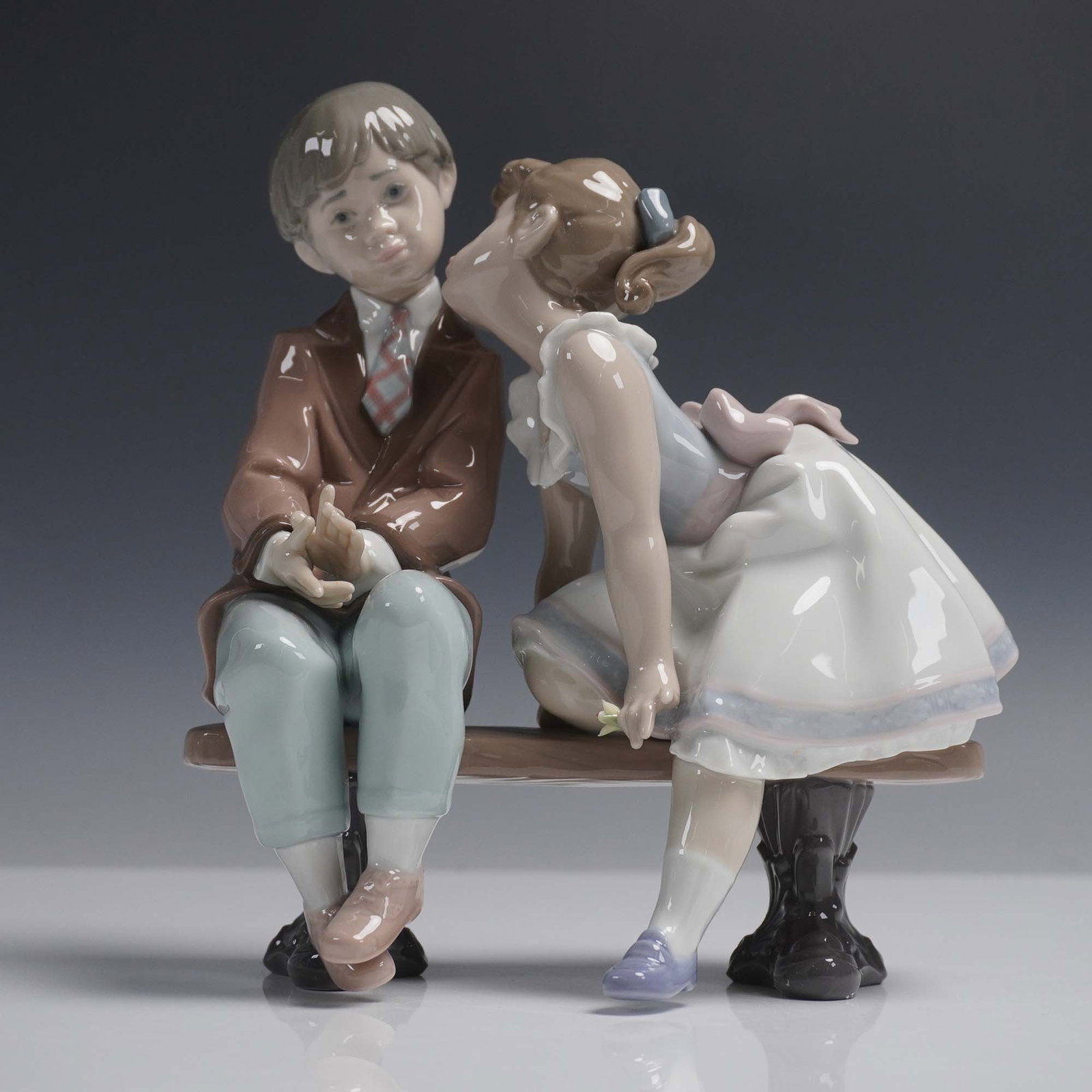 Ten and Growing 1007635 - Lladro Porcelain Figurine: This Lladro figurine, Ten and Growing, was released to commemorate the 10th anniversary of the Lladro Collectors Society. It depicts a young girl giving a shy boy a kiss on the cheek as they sit toget