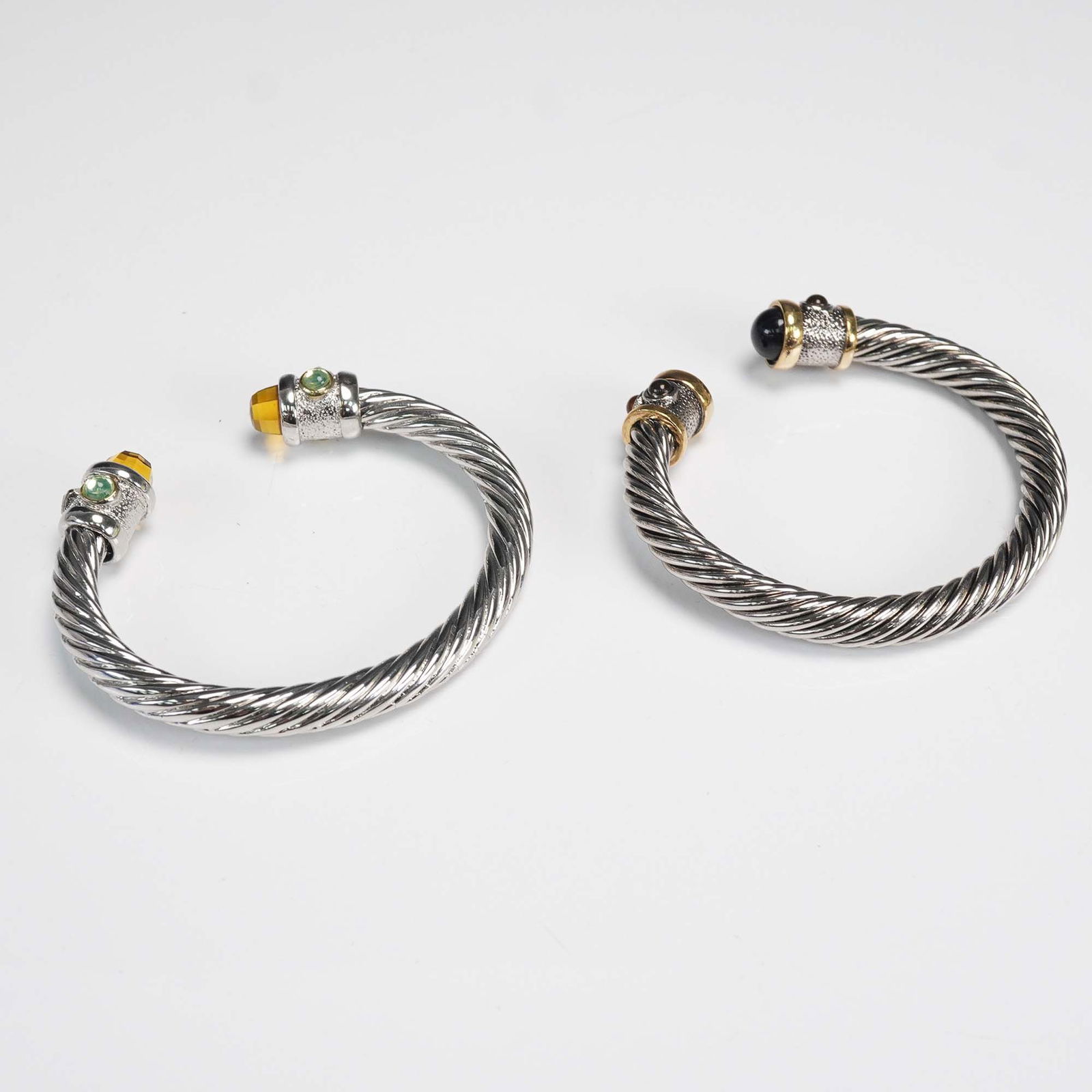 2pc Silver-Tone Cable Cuff Bracelets with Multicolor Accents: Pair of cable-style cuff bracelets featuring twisted silver-tone metal bands with embellished ends. One bracelet is accented with domed black stones and smaller amber cabochons set in gold-tone mounts