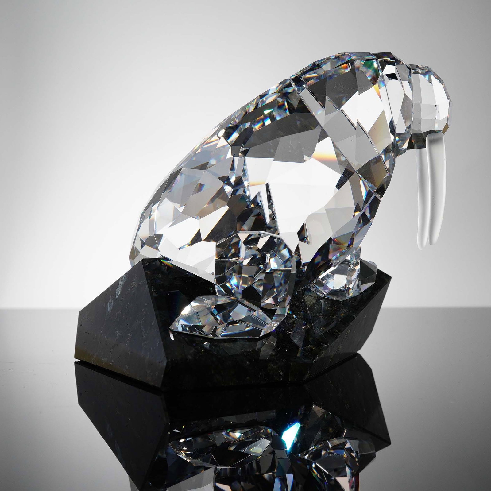 Swarovski Crystal Figurine, Walrus on Stone Base: This striking Swarovski Soulmates Walrus figurine, introduced in 2007, features a faceted clear crystal body with smooth frosted tusks, resting on a gleaming black granite base. Designed by Mario Dili